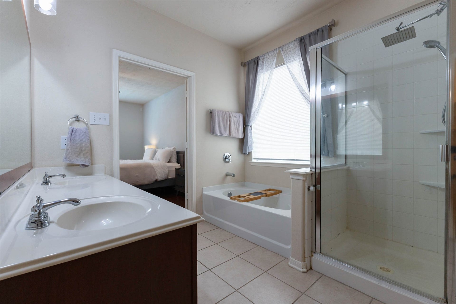 An alternate view of the primary bath highlights the soaking tub positioned beneath a large window and the separate glass-enclosed shower, creating distinct spaces for both relaxation and everyday convenience.