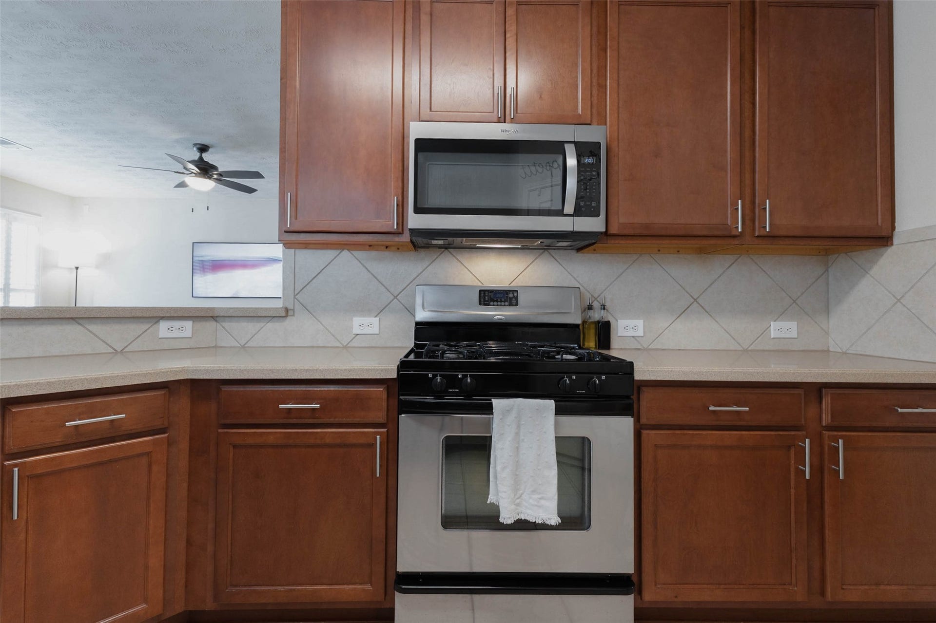 Rich wood cabinetry frames the main cooking area, where a stainless steel gas range and built-in microwave provide a streamlined focal point. Neutral countertops and tile backsplash complement the warm cabinetry for a classic, inviting finish.