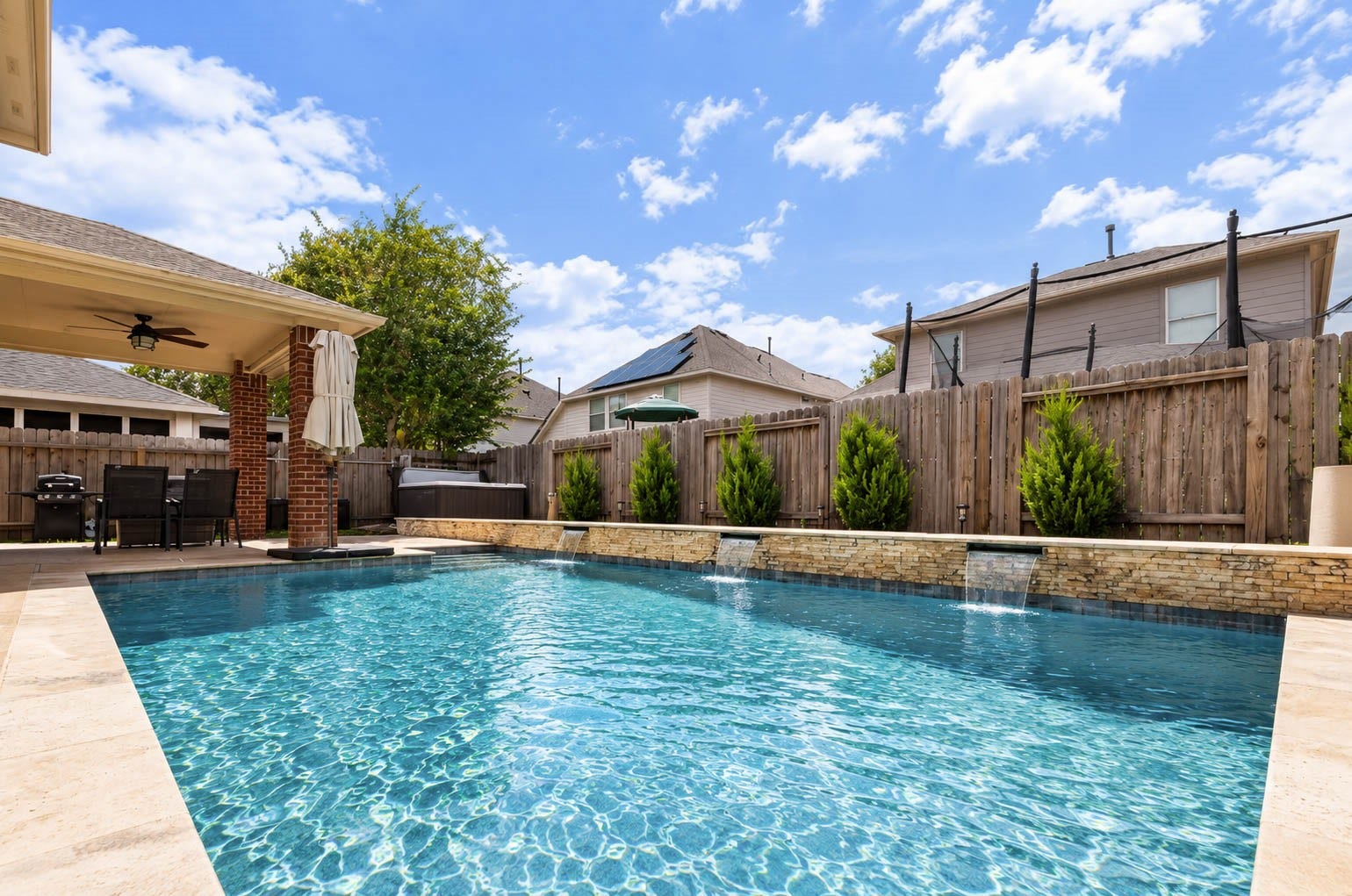 Sparkling water, cascading features, and a covered entertaining area come together to create an inviting backyard retreat. A privacy fence encloses the yard, while the covered patio and nearby spa (negotiable) expand the possibilities for year-round outdoor enjoyment.