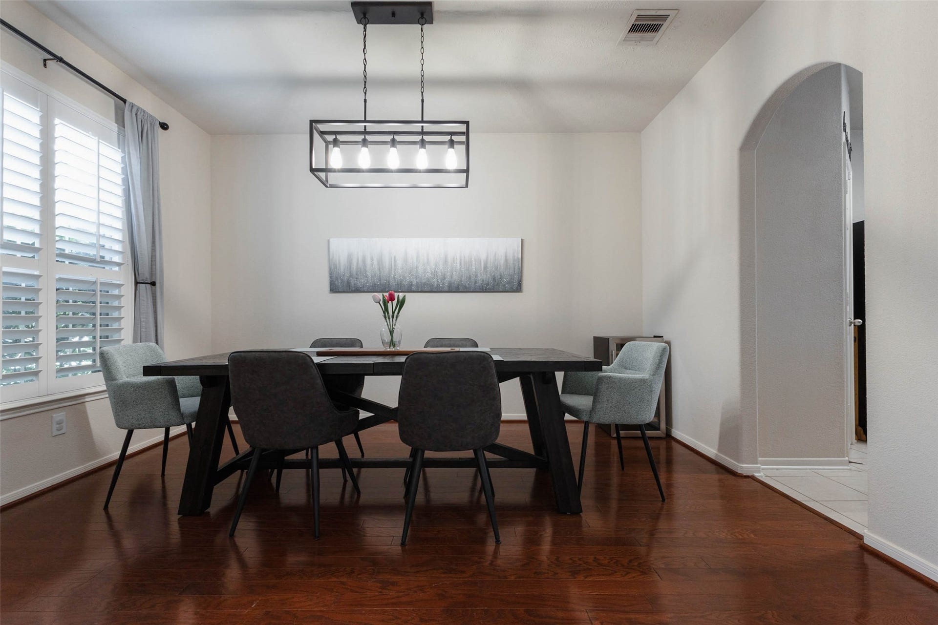 The formal dining room offers an elegant setting for intimate dinners and larger gatherings alike. Rich wood flooring, oversized windows with plantation shutters, and a statement light fixture give the room a polished look, while convenient kitchen access makes entertaining effortless.