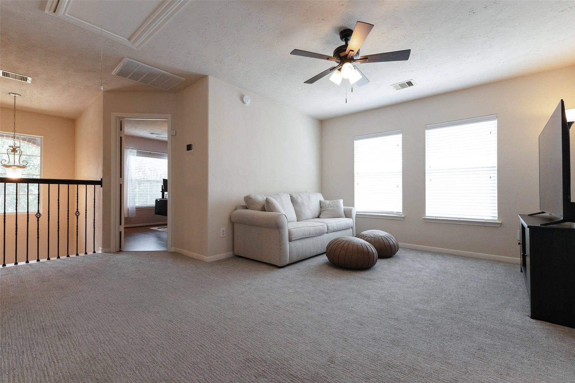 The spacious upstairs game room creates a comfortable second living area with plush carpeting, a ceiling fan, and abundant natural light from multiple windows. Its generous proportions provide plenty of flexibility for lounging, gaming, movies, or play.