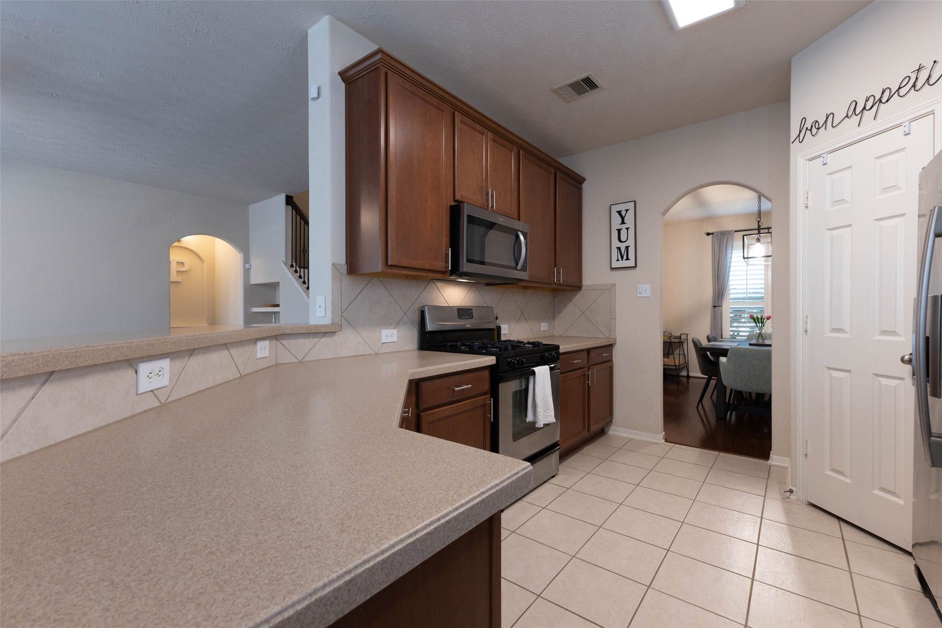 Designed with everyday functionality in mind, the kitchen offers generous stretches of counter space, abundant upper and lower cabinetry, stainless steel appliances, and a neutral diagonal-set tile backsplash. The raised counter also keeps the kitchen visually connected to the adjoining living areas.