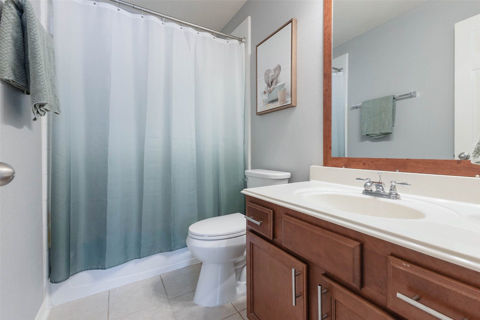 The secondary full bathroom features a long vanity with warm wood cabinetry, a large framed mirror, tile flooring, and a tub/shower combination.