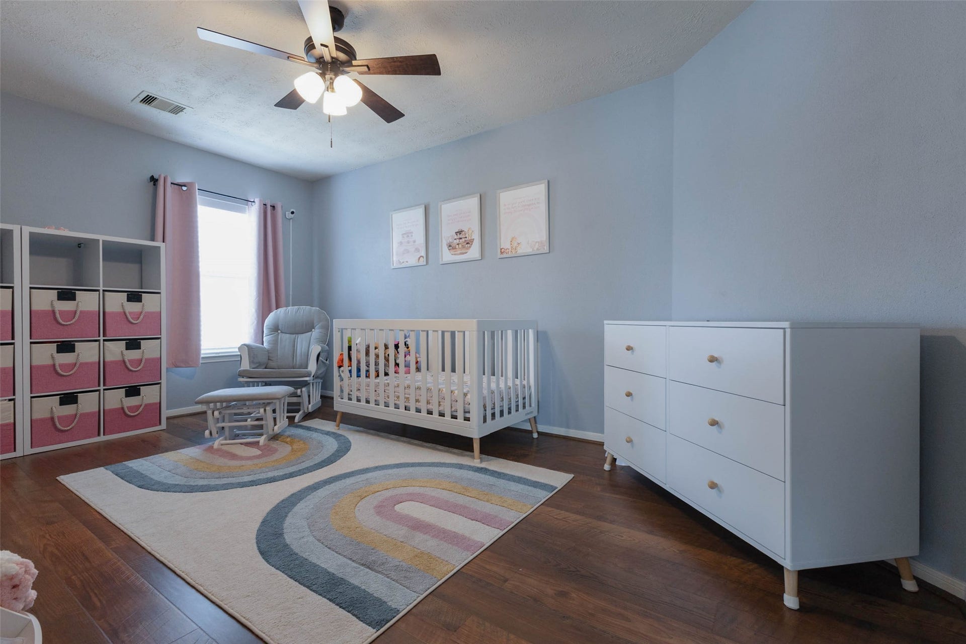 This charming secondary bedroom is currently styled as a nursery and offers wood-look flooring, a ceiling fan, and plenty of room for bedroom furnishings. Soft natural light creates a comfortable setting that can easily evolve as needs change.