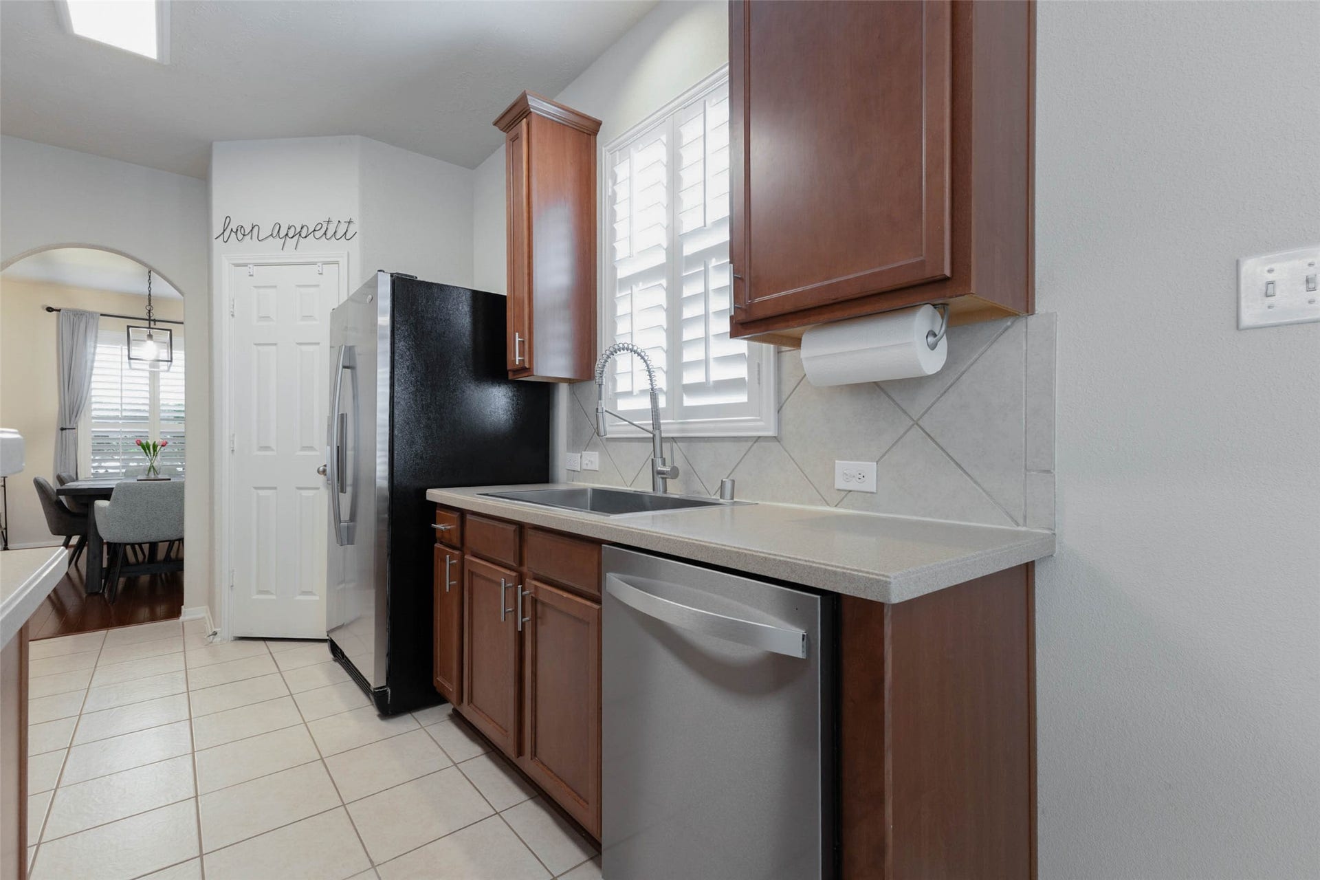 The opposite side of the kitchen provides another generous work zone with additional cabinetry and counter space surrounding the sink. Plantation shutters bring natural light over the workspace, while the stainless steel dishwasher was replaced in 2026 and is noted by the sellers as a quiet 47 dBA model.