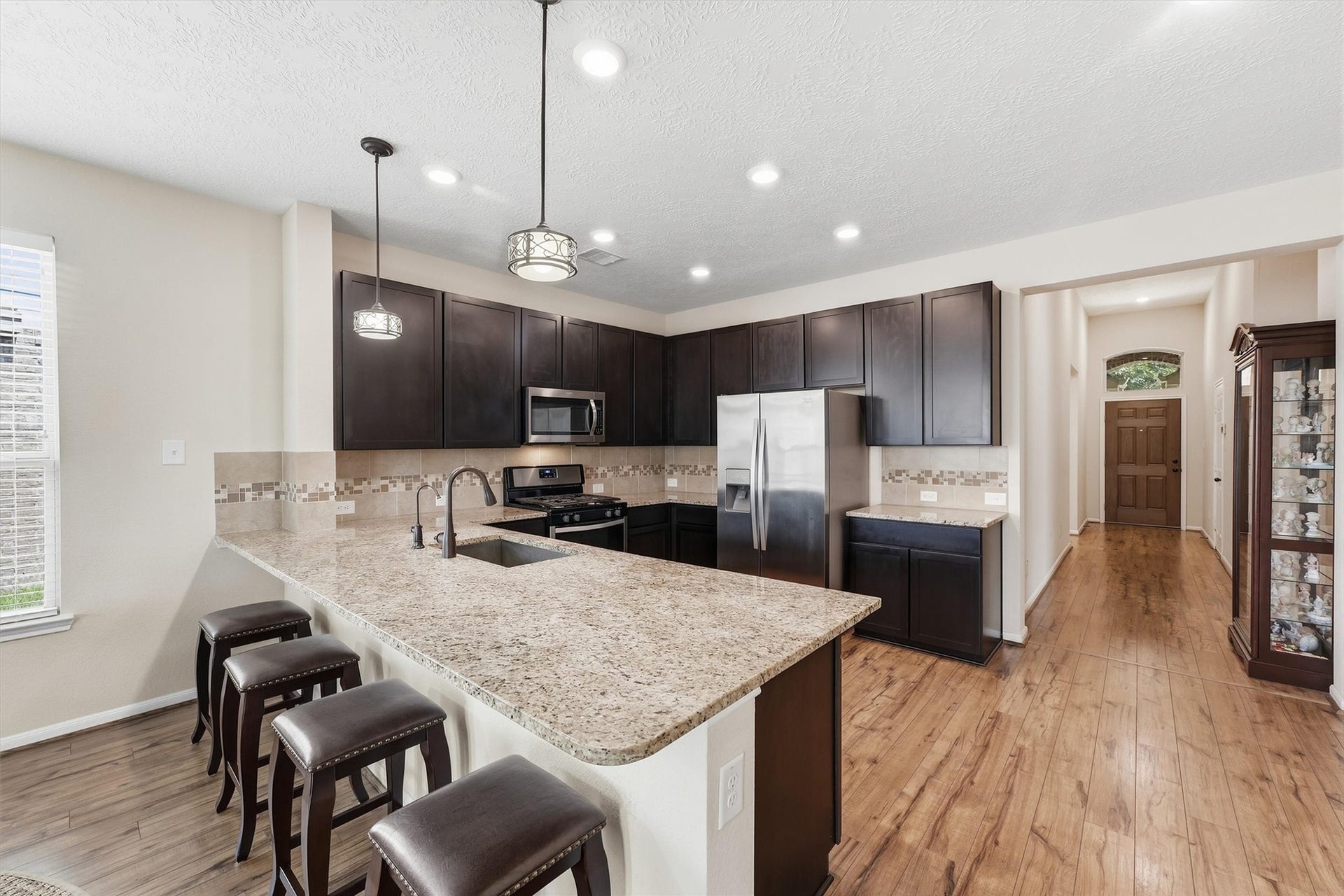 25522 Brentmoor Drive, Porter, TX 77365 Spacious island kitchen boasting rich dark cabinetry, stainless steel appliances, granite countertops, modern pendant lighting, and warm wood-look floors.