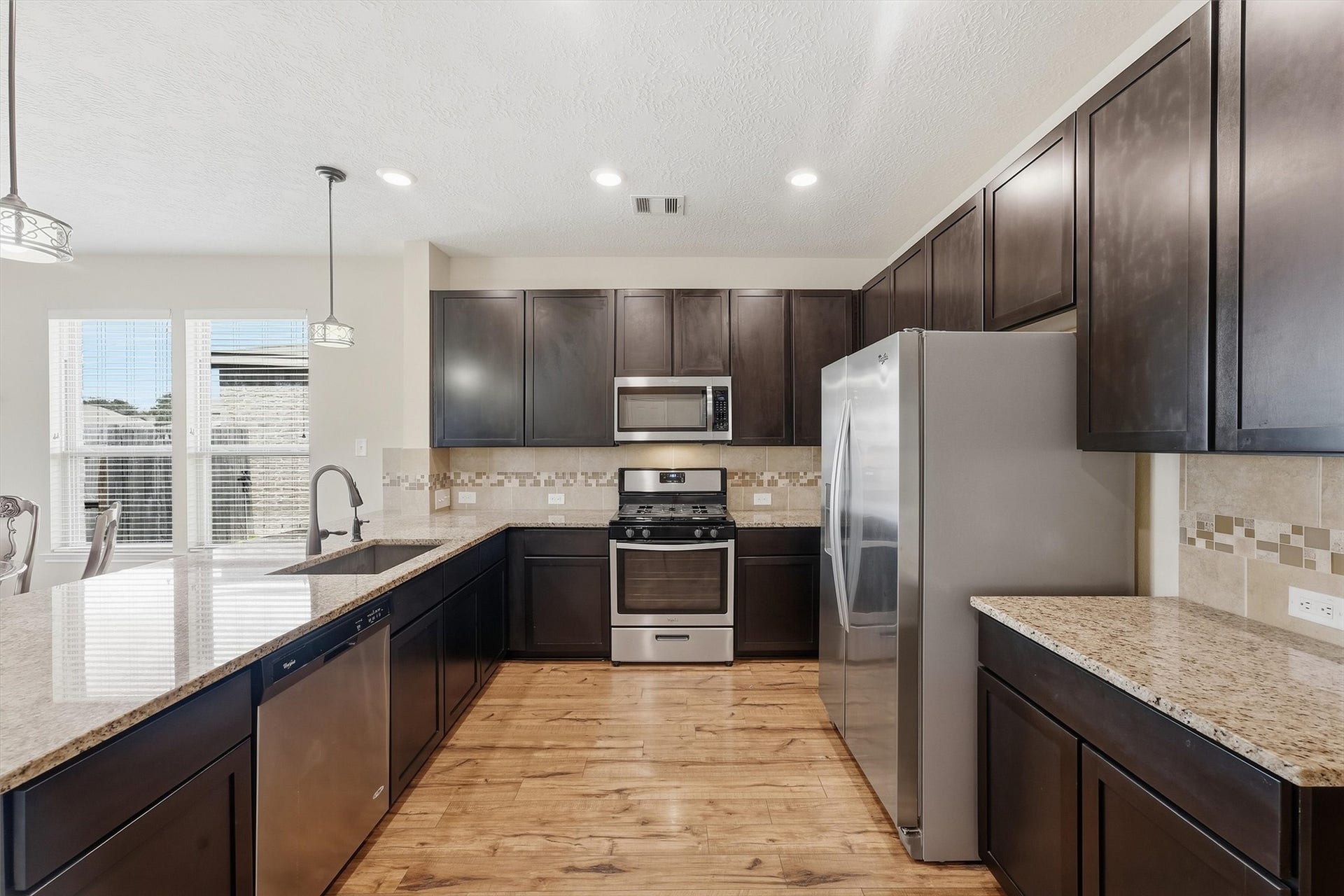 25522 Brentmoor Drive, Porter, TX 77365 Spacious island kitchen boasting rich dark cabinetry, stainless steel appliances, granite countertops, modern pendant lighting, and warm wood-look floors.