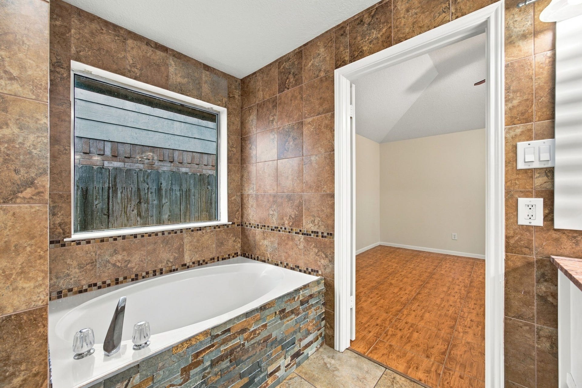 12902 Sandri Lane, Houston, TX 77077 Positioned beneath a window, the soaking tub features a stacked-stone surround and decorative tile accents.