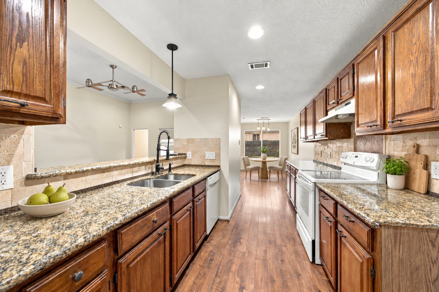 12902 Sandri Lane, Houston, TX 77077 The kitchen features wood cabinetry, granite countertops, a tile backsplash, and a sink overlooking the living area. Virtually staged