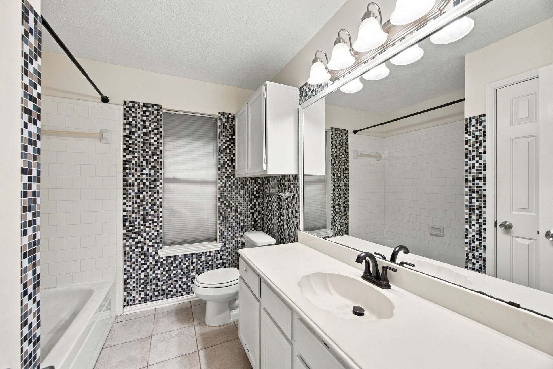 12902 Sandri Lane, Houston, TX 77077 Mosaic tile accents add character to this bathroom, featuring a wide vanity, a large mirror, and a tub/shower combination.