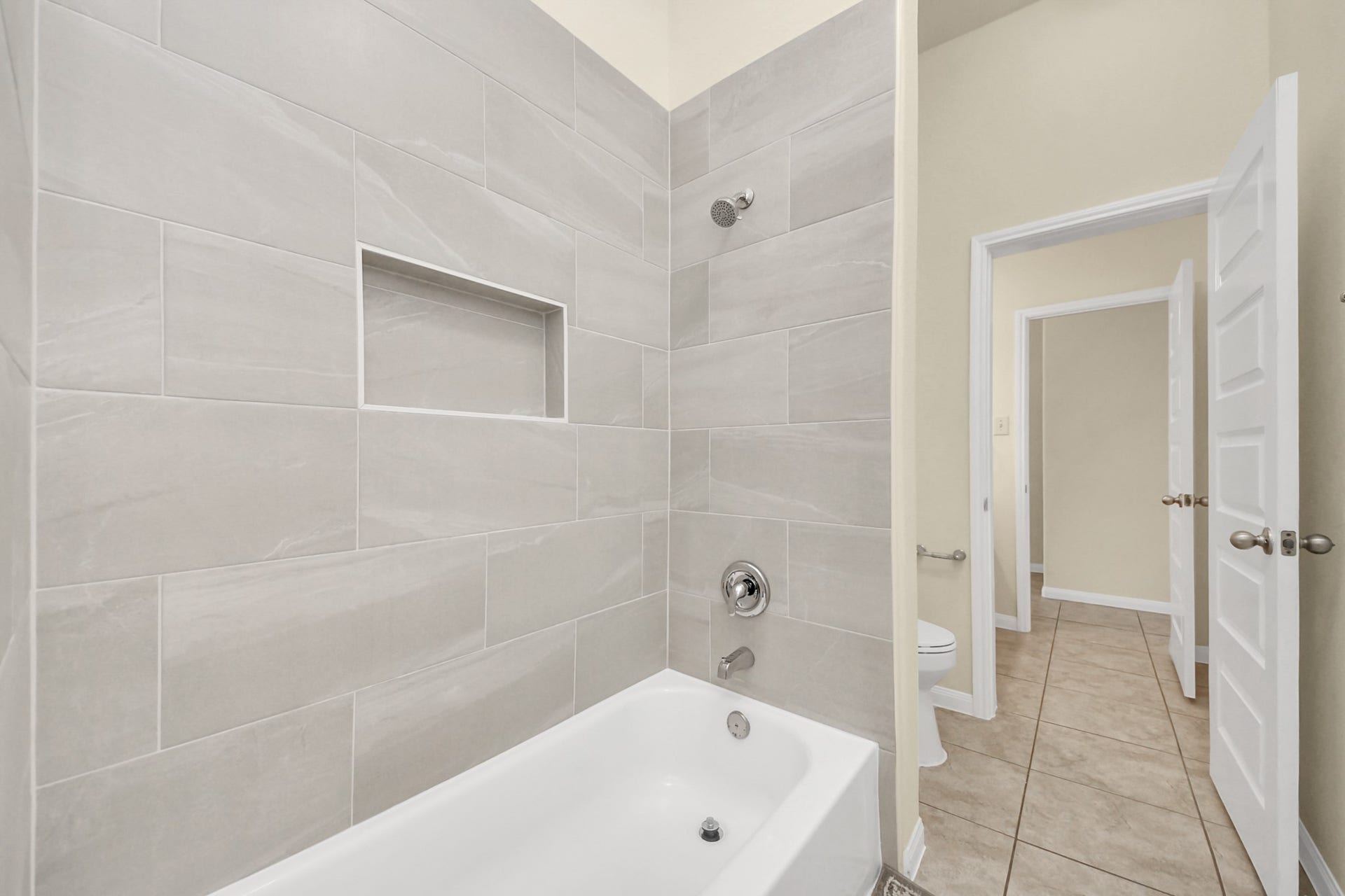 12906 Millstream Bend Lane, Tomball, TX 77377 Sleek bathroom featuring a modern bathtub with elegant gray tile surround, built-in shelf, and access to a bright hallway.