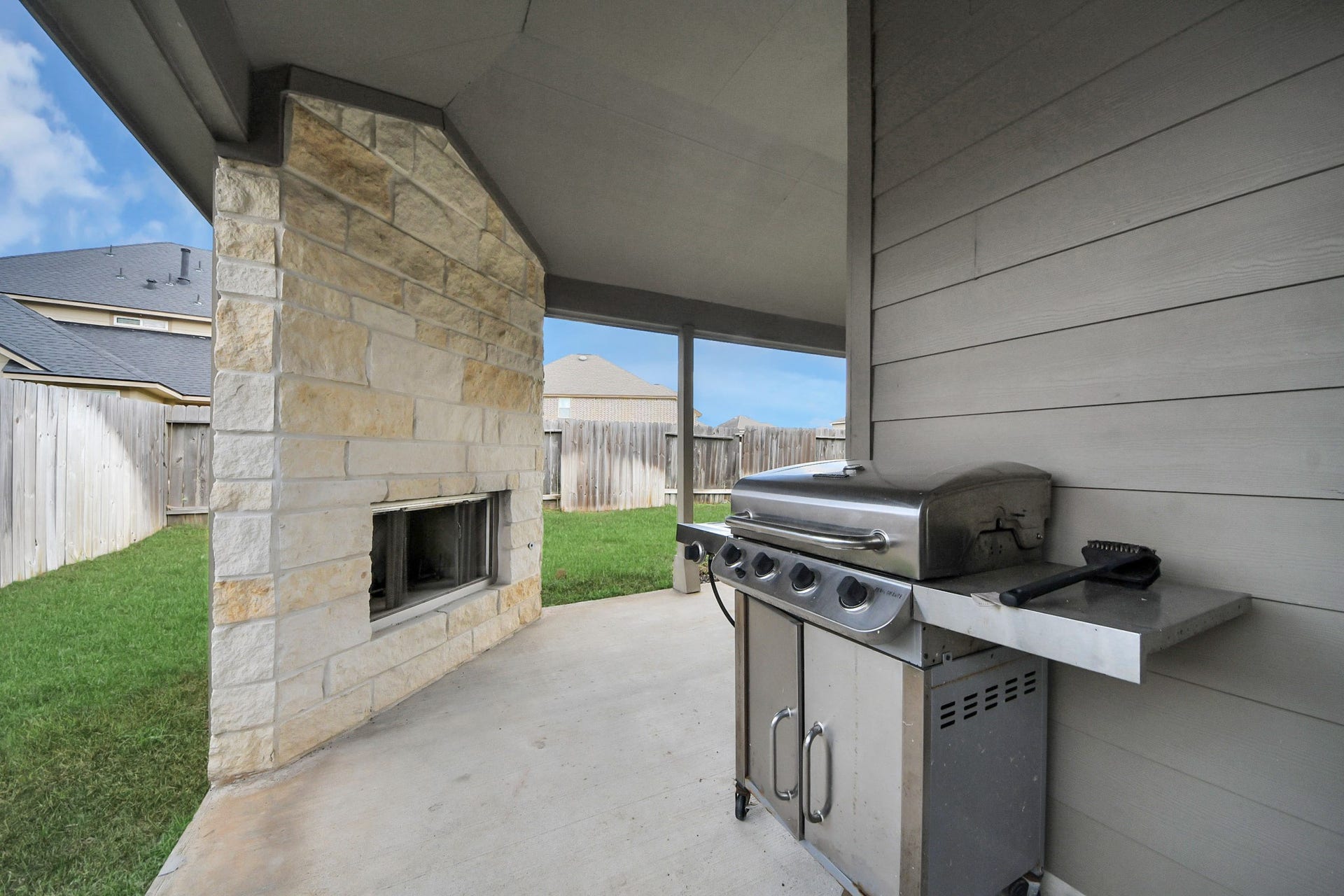 12906 Millstream Bend Lane, Tomball, TX 77377 Covered patio with a built-in stone fireplace and a stainless steel grill, perfect for outdoor entertaining.