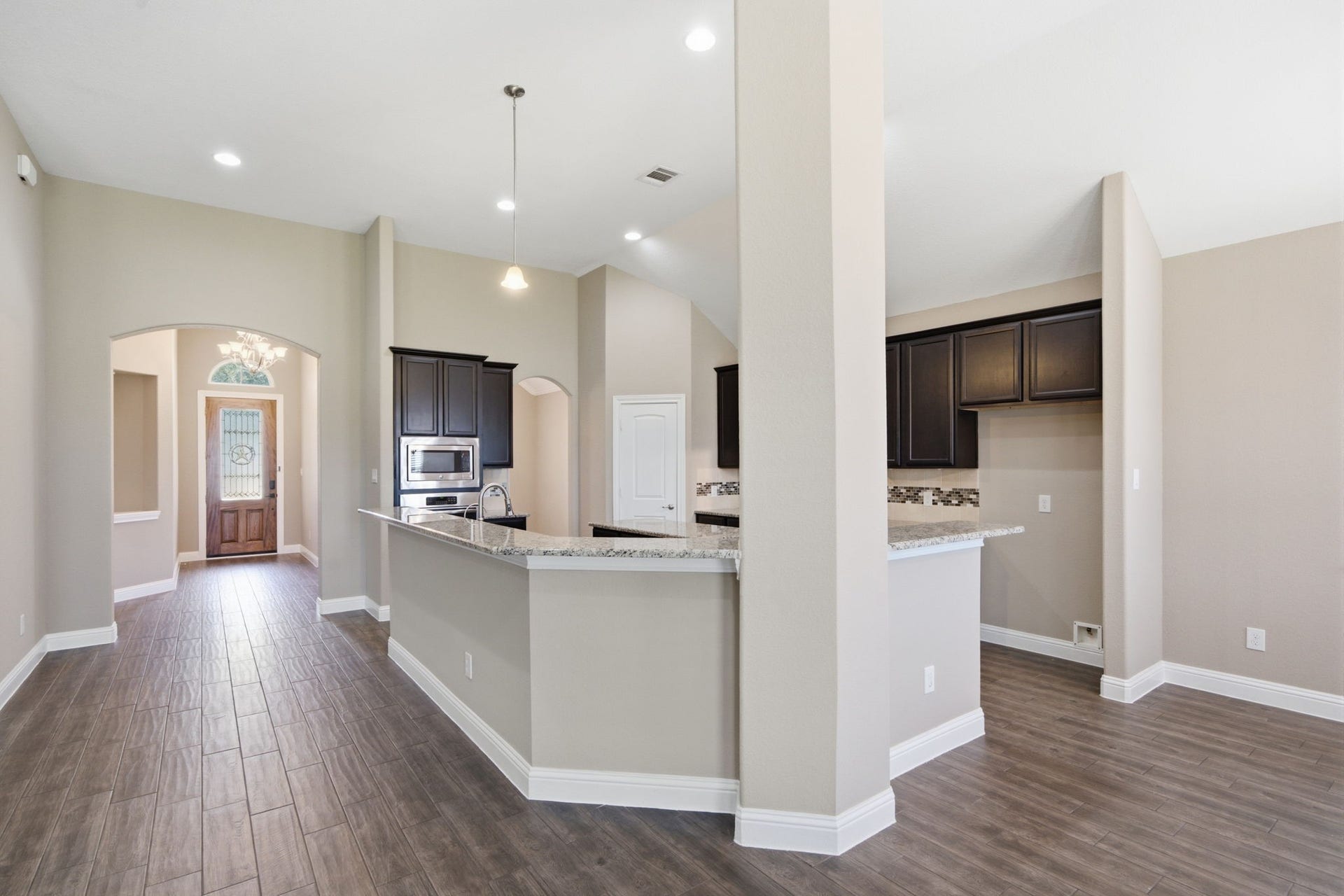 18818 Wichita Trail, Magnolia, TX 77355 Open-concept layout flows effortlessly from the tiled foyer past a raised breakfast bar and into the kitchen and living spaces. High ceilings, neutral wall tones, and dark cabinetry create a striking contrast in this functional single-story design.