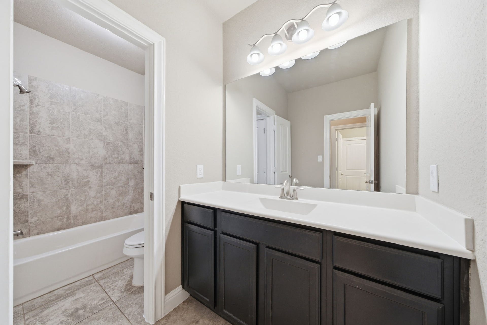 18818 Wichita Trail, Magnolia, TX 77355 Secondary bath features a functional tub and shower combo with neutral tile surround and classic plumbing fixtures. A wide vanity with rich dark cabinetry, a white countertop, and a large mirror completes the space.