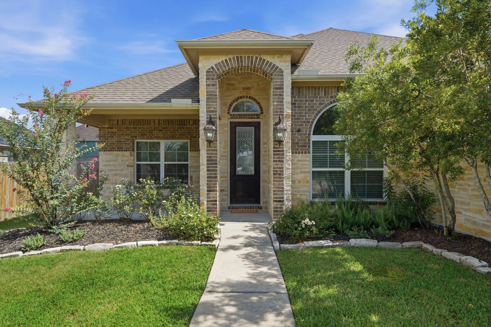 18818 Wichita Trail, Magnolia, TX 77355 A concrete walkway leads straight to the grand stone archway of the front patio, highlighting the striking combination of brick and stone on the facade of this one-story residence.