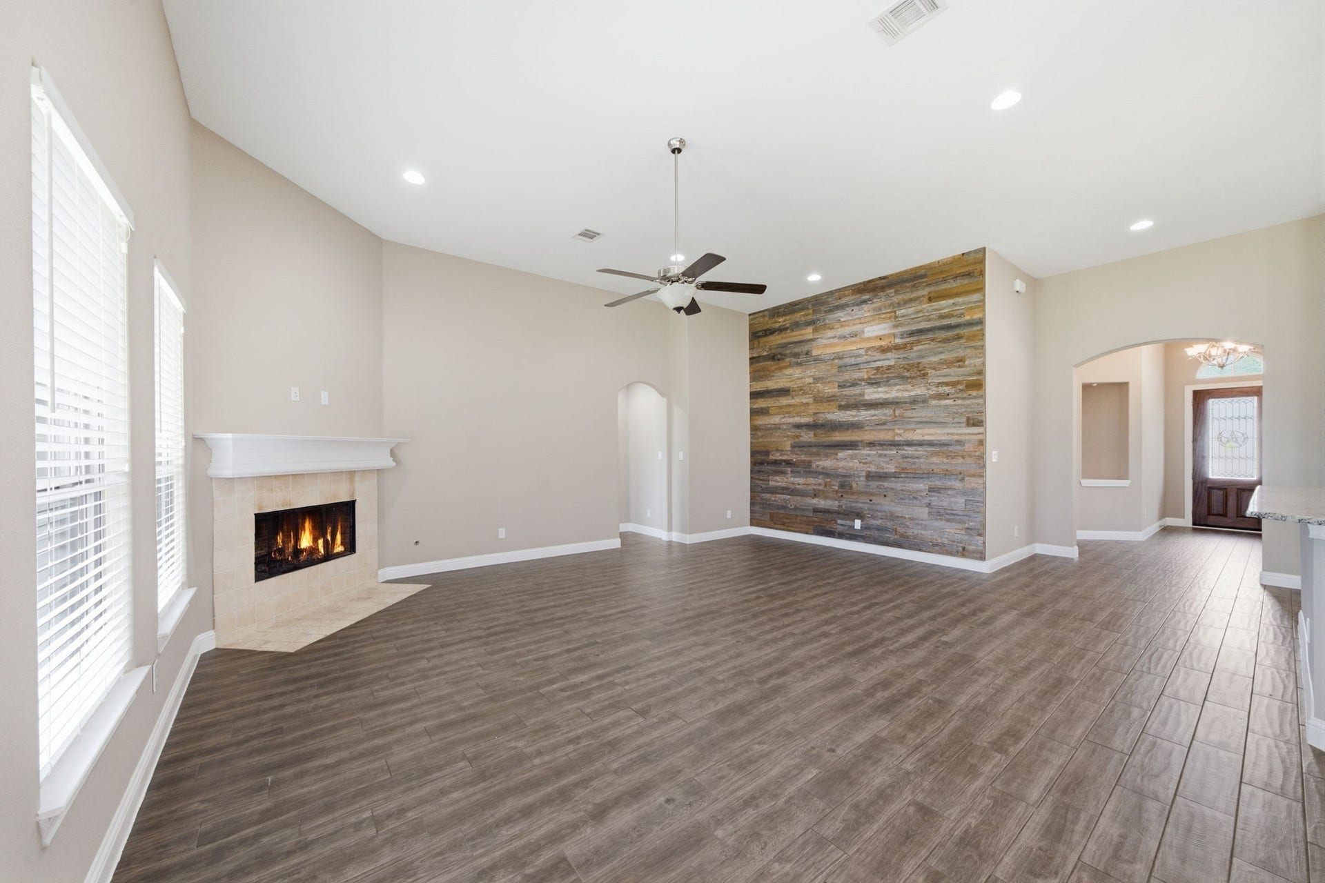 18818 Wichita Trail, Magnolia, TX 77355 Expansive living room features a spacious, open layout, a cozy corner fireplace, and sleek plank flooring. The eye-catching wood accent wall adds architectural interest, while wide windows provide plenty of space for seating and effortless patio access.