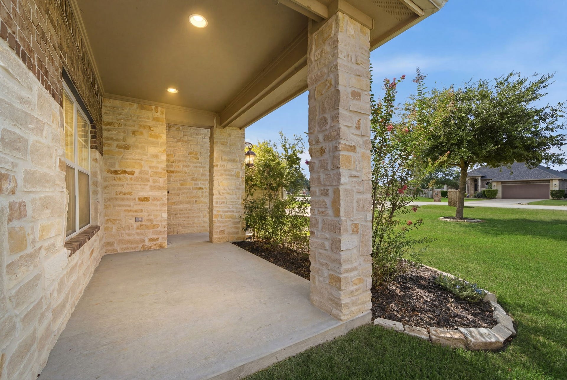 18818 Wichita Trail, Magnolia, TX 77355 A covered front patio features robust stone columns and recessed lighting, offering a welcoming entryway with a clear view of the manicured lawn.