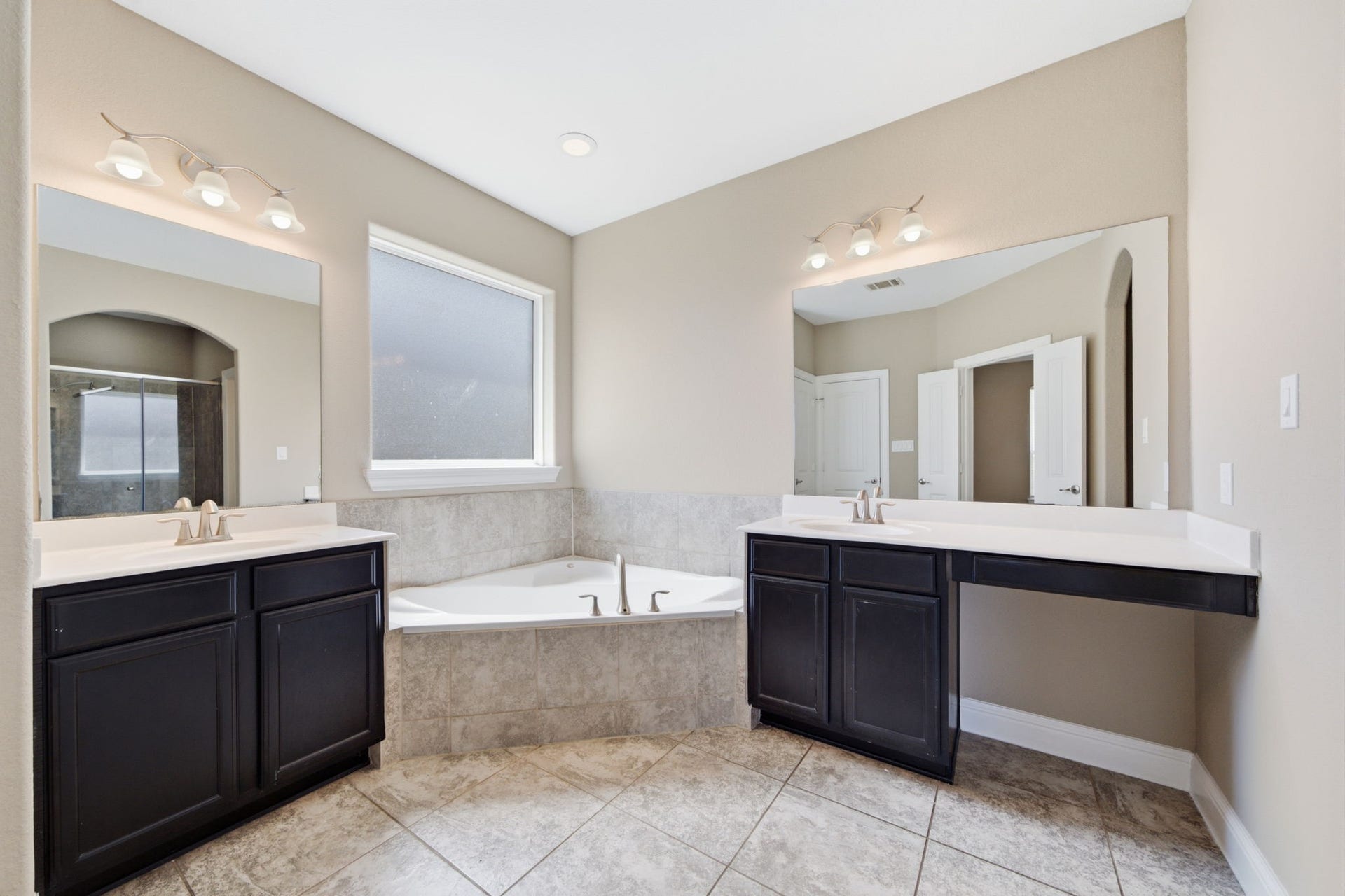 18818 Wichita Trail, Magnolia, TX 77355 Spa-inspired primary bathroom features dual vanities with dark cabinetry and a built-in makeup vanity. Nestled between the vanities, a deep spa jetted tub with tile surround sits beneath a frosted window, offering a peaceful space to unwind.