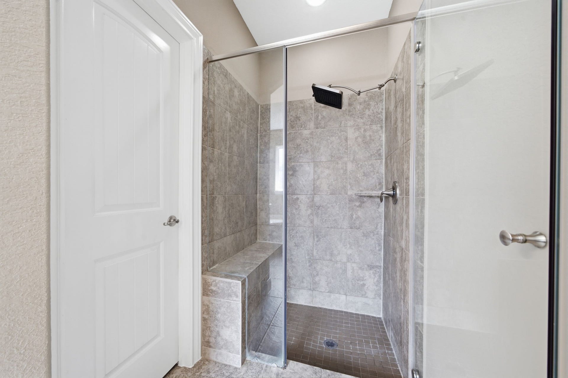 18818 Wichita Trail, Magnolia, TX 77355 Glass-enclosed shower showcases neutral tile walls, a built-in bench, and a modern square showerhead.