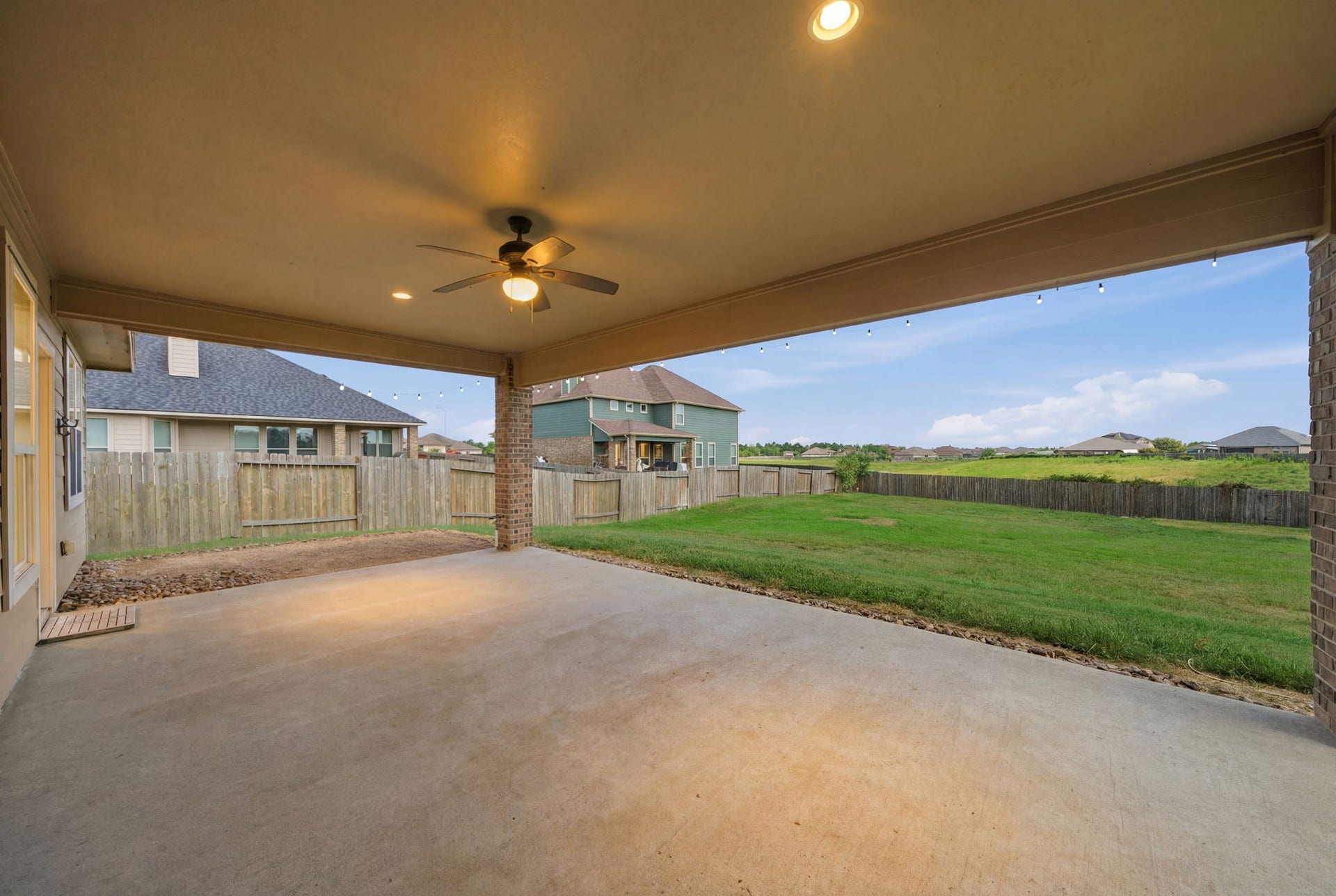 18818 Wichita Trail, Magnolia, TX 77355 This spacious covered patio features a sturdy brick pillar and expansive concrete slab. Festive string lights accent the roofline, framing peaceful views of the vast green lawn and open landscape beyond. The oversized backyard offers ample space and an exciting opportunity to add a future pool.