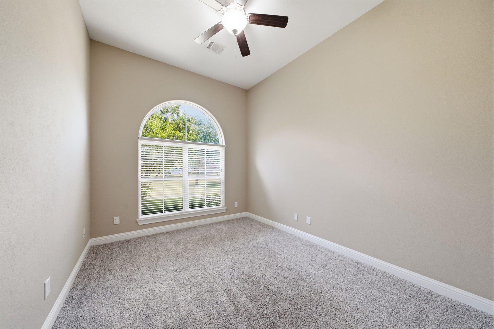 18818 Wichita Trail, Magnolia, TX 77355 Flooring of soft carpet and an impressive arched window define this secondary bedroom on the first floor. High ceilings with a classic fan-light fixture and neutral wall paint enhance the open, airy layout.