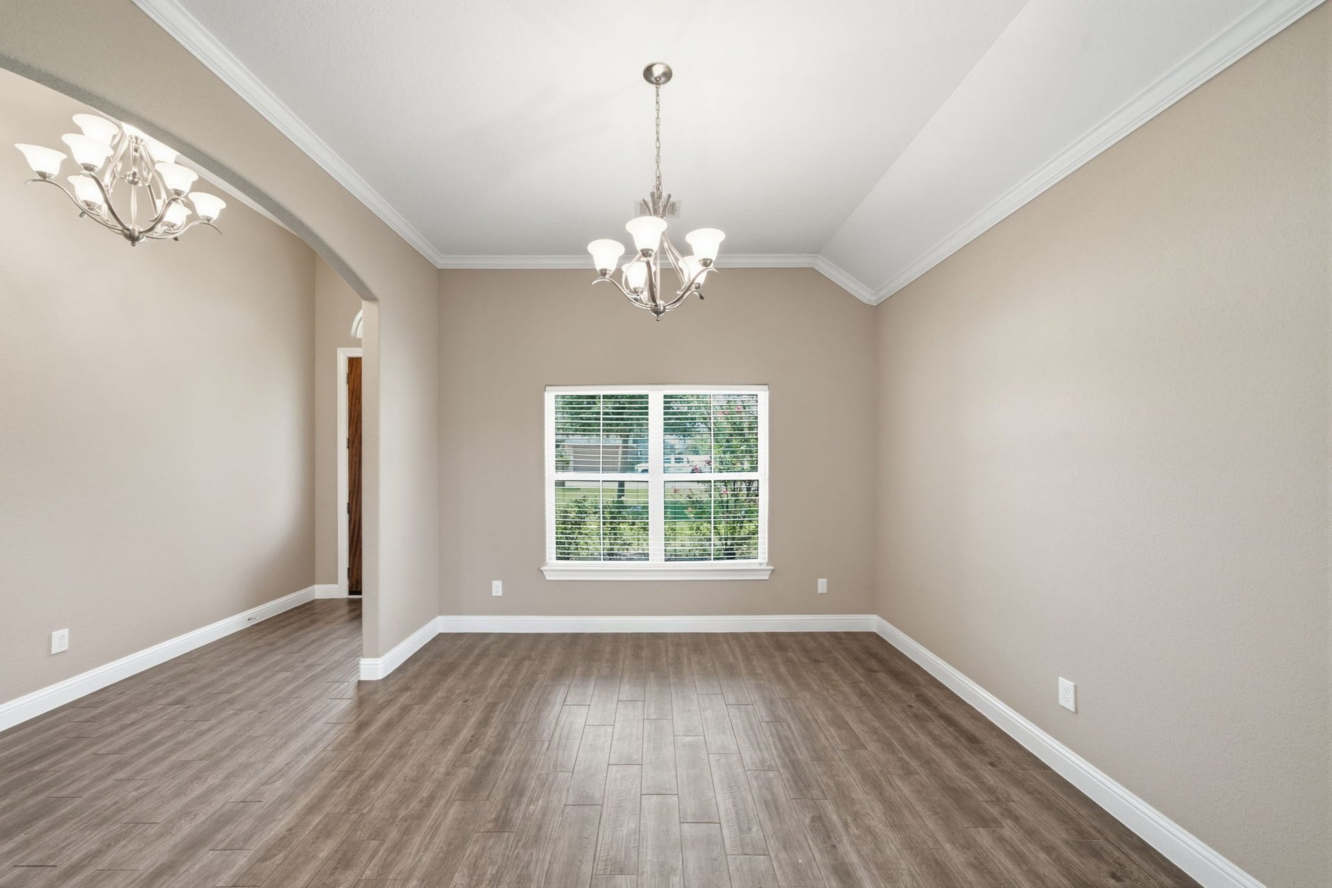 18818 Wichita Trail, Magnolia, TX 77355 Elegant formal dining room showcases a high vaulted ceiling, neutral wall paint, and durable wood-look tile flooring. The open layout accommodates a large dining table, while a wide front window with blinds provides an inviting view of the yard.