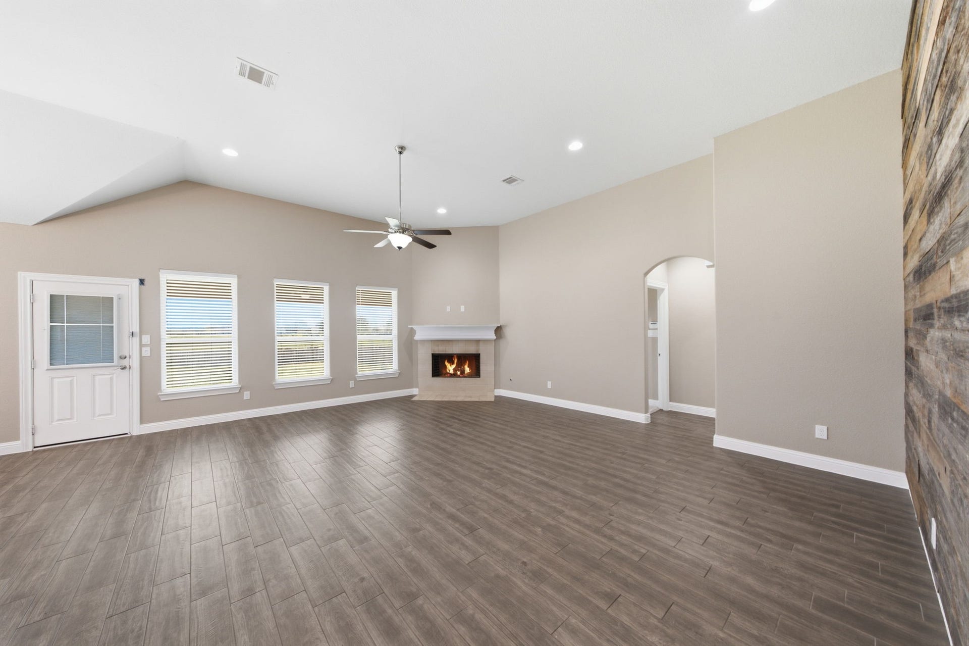 18818 Wichita Trail, Magnolia, TX 77355 Spacious living room showcases a cozy corner fireplace, vaulted ceilings, and durable wood-look tile flooring. Trios of large windows allow natural light to fill the open space, while a glass-paneled door provides easy access to the backyard.
