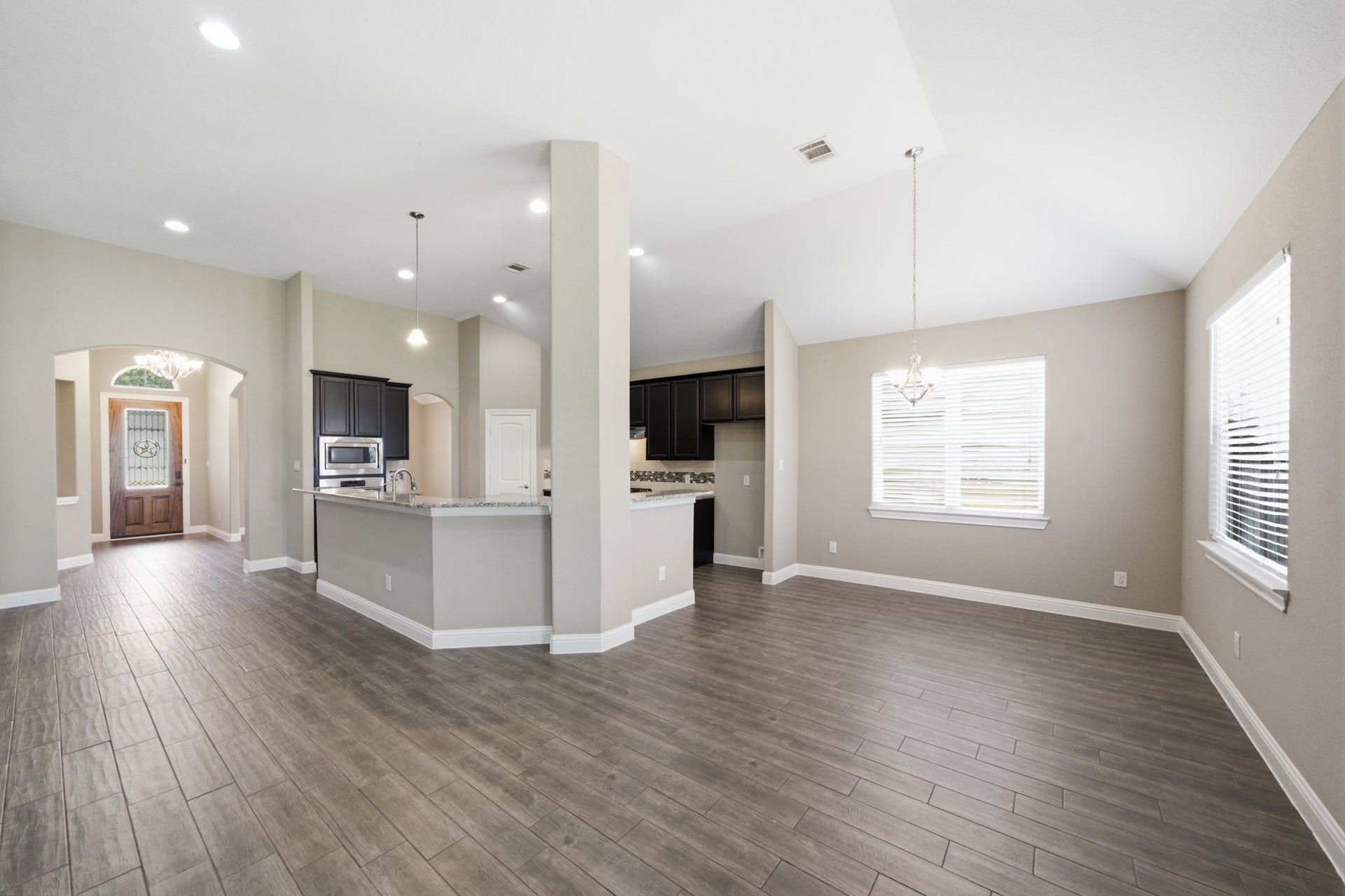 18818 Wichita Trail, Magnolia, TX 77355 Open layout effortlessly connects the tiled foyer, kitchen breakfast bar, and open-concept dining area. High vaulted ceilings, dark cabinetry, and durable wood-look tile flooring create a spacious and cohesive look throughout these central living spaces.
