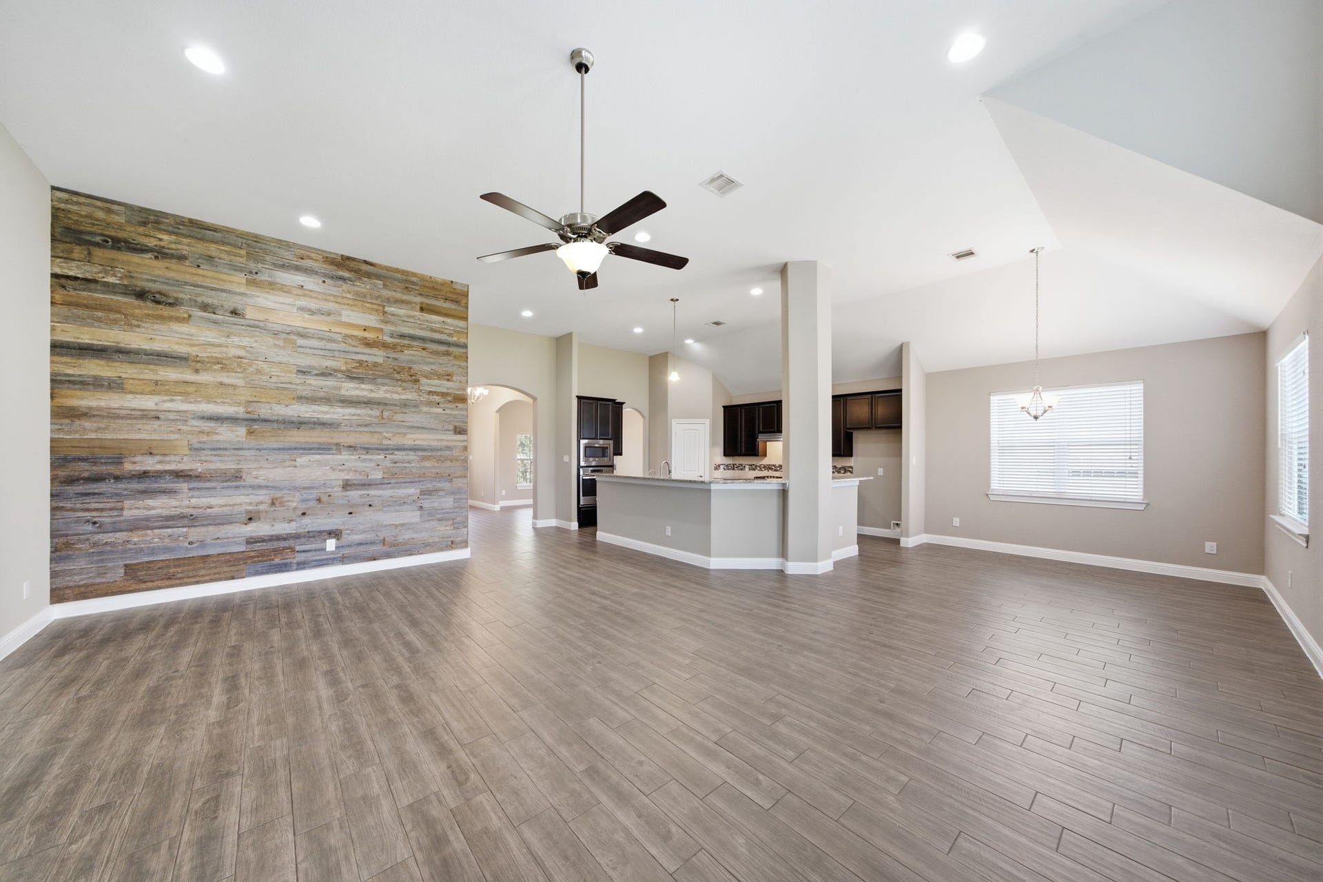 18818 Wichita Trail, Magnolia, TX 77355 Featuring an expansive open-concept layout, this light-filled main living space showcases an eye-catching wood plank accent wall, soaring ceilings, and durable tile flooring. The seamless design flows effortlessly from the living room into the kitchen and dining areas, providing a spacious setting for daily life.