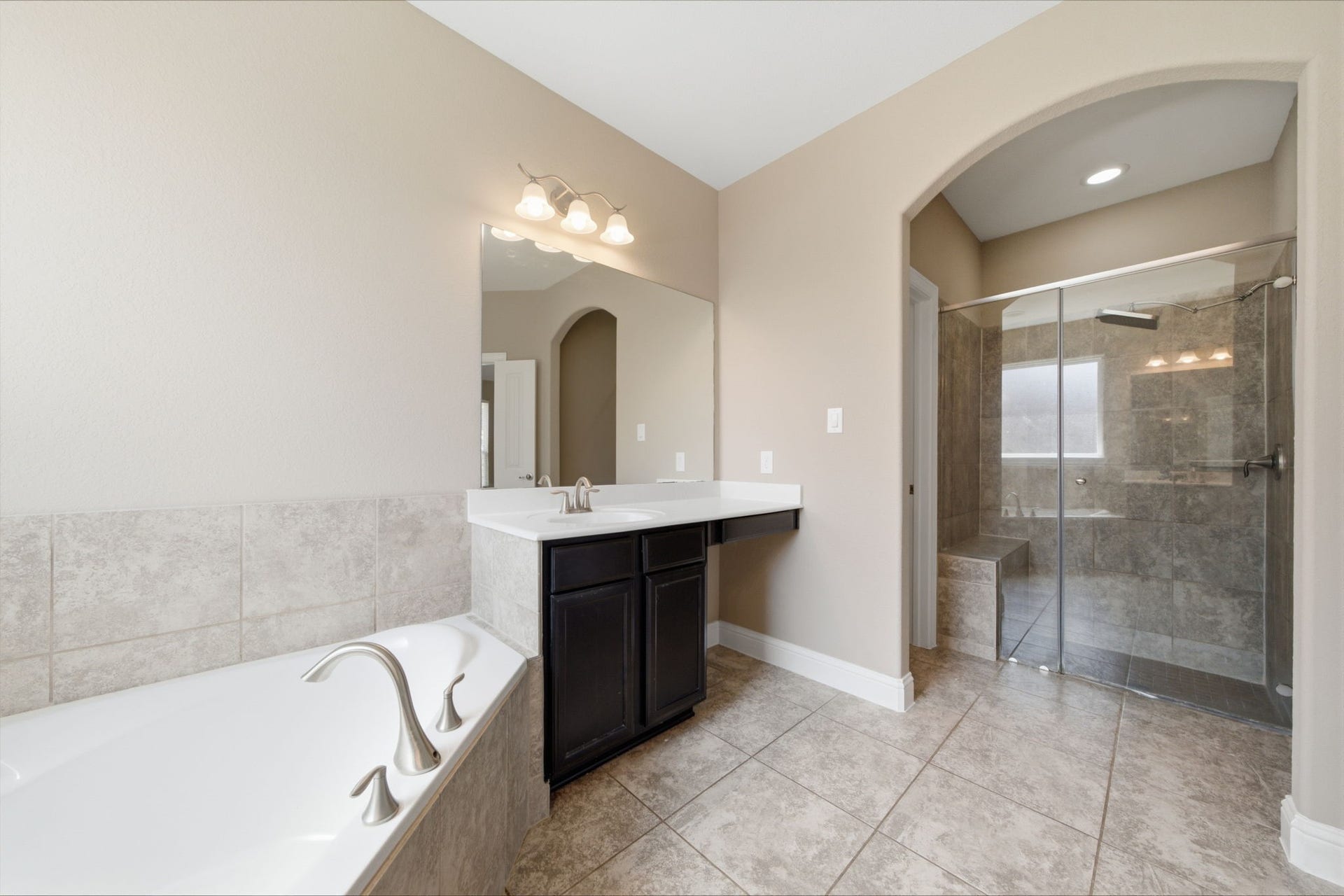 18818 Wichita Trail, Magnolia, TX 77355 Spa-like primary bath features a glass-enclosed shower, a deep soaking tub, and a vanity with rich dark cabinetry. Warm tile flooring and an elegant arched entryway complete the relaxing layout.