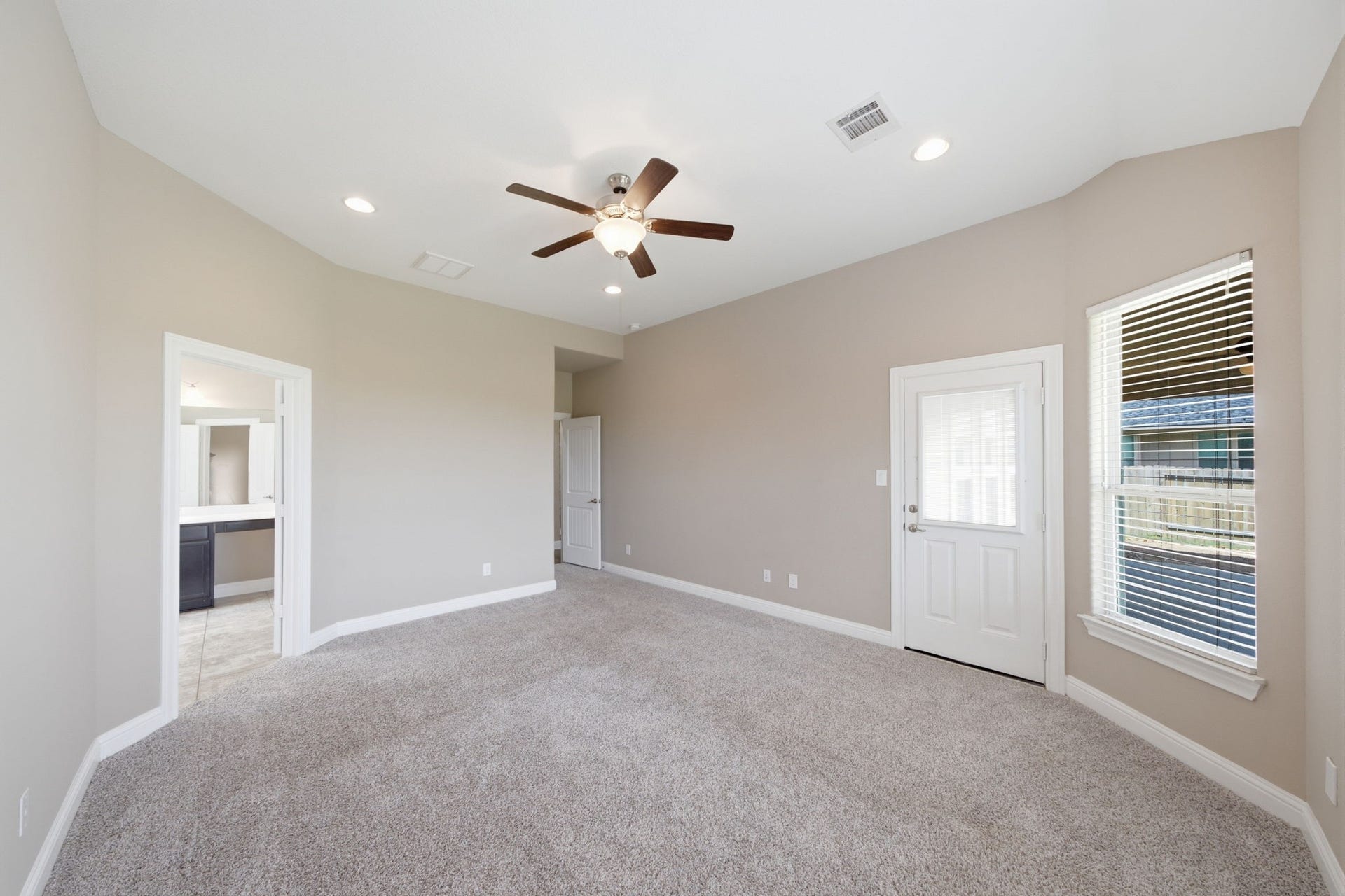 18818 Wichita Trail, Magnolia, TX 77355 Expansive primary suite on the first floor showcases plush carpet flooring, a classic ceiling fan, and neutral paint. Direct access to the backyard and a wide window with blinds provide peaceful views of the private fenced yard.