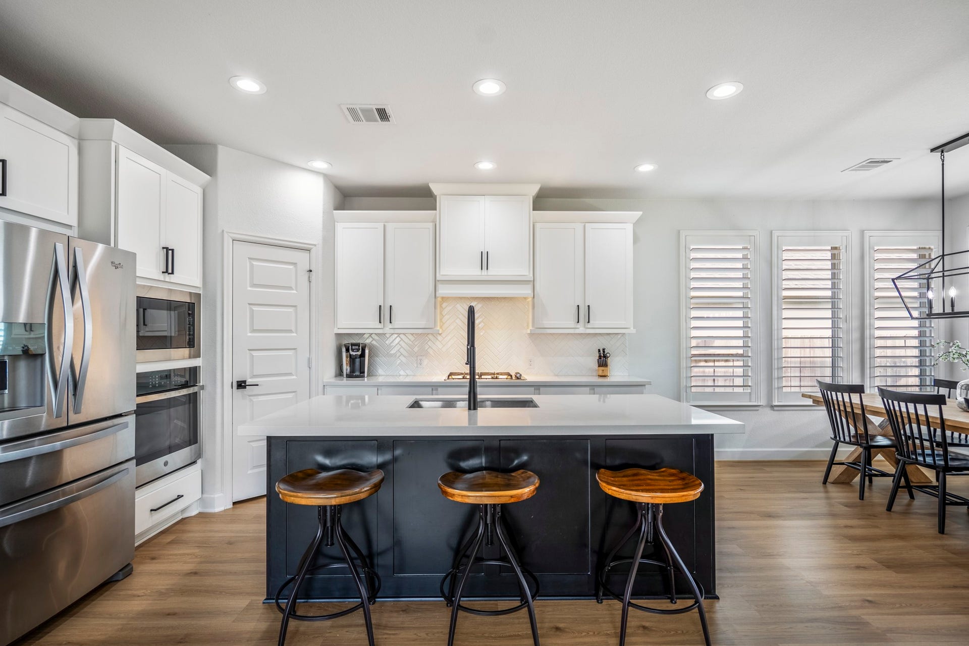 304 Mullins Court, Montgomery, TX 77316 This modern kitchen features sleek stainless steel appliances, white cabinetry, and a spacious island with seating. The open layout includes a dining area with large windows, providing ample natural light and a cozy, inviting atmosphere.