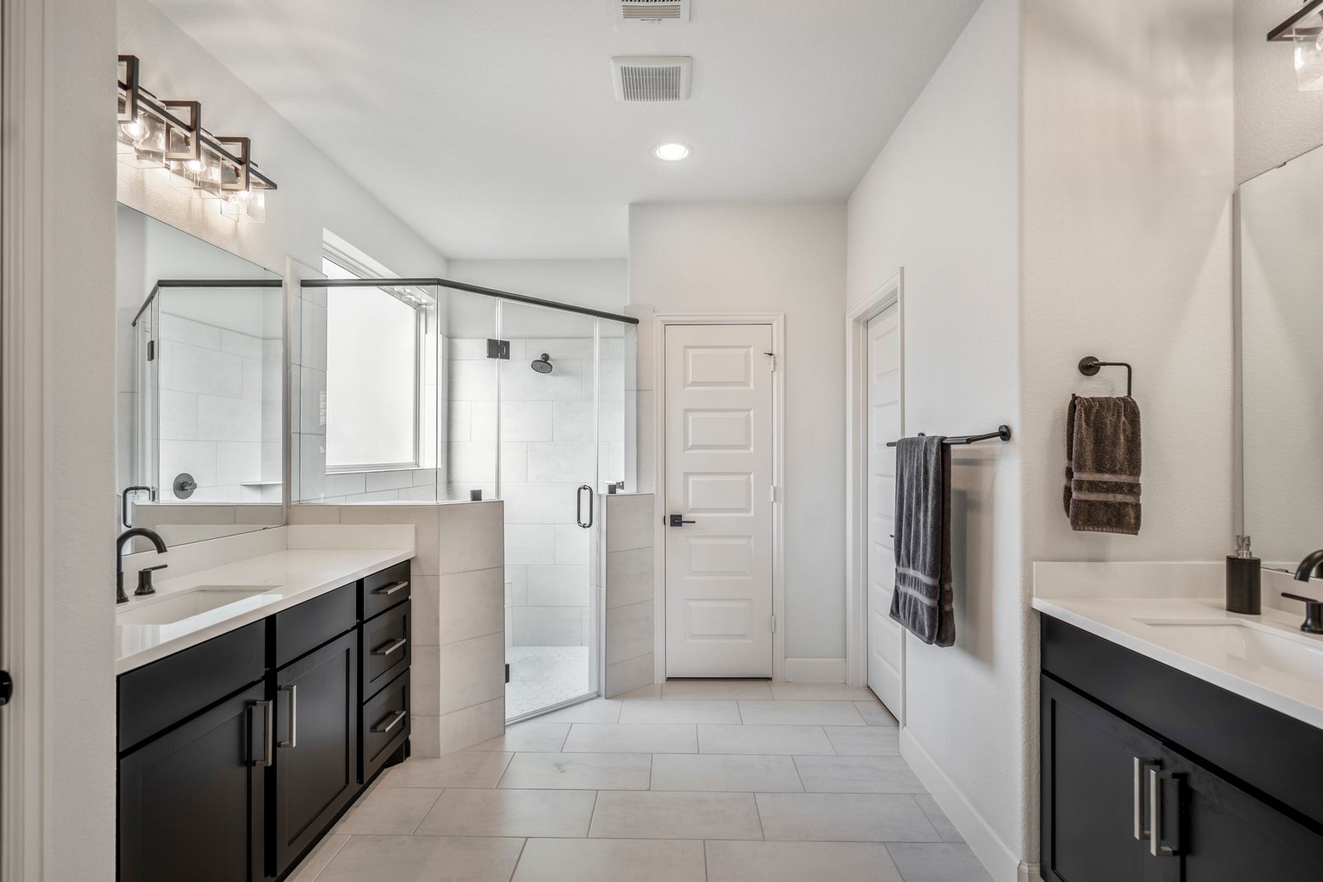 304 Mullins Court, Montgomery, TX 77316 This modern primary bathroom features dual vanities with sleek black cabinets, a spacious glass-enclosed shower, and elegant lighting fixtures, all set against crisp white walls and tile flooring.
