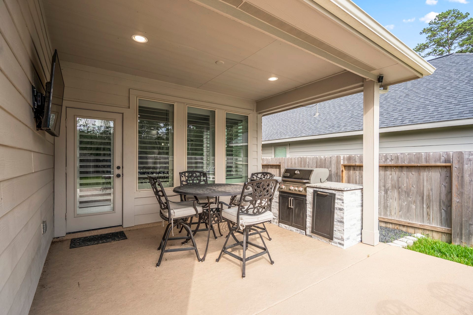 304 Mullins Court, Montgomery, TX 77316 This photo showcases a cozy covered patio with a built-in grill, outdoor seating, and a mounted TV, perfect for entertaining or relaxing.