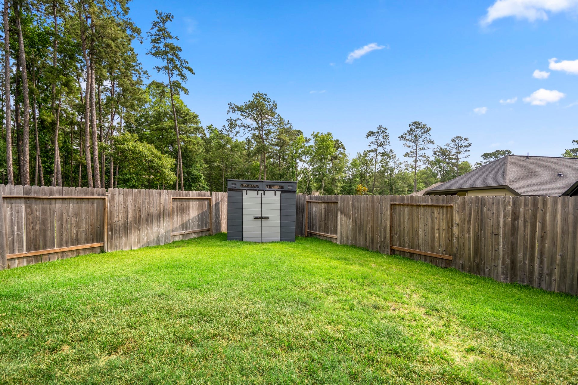 304 Mullins Court, Montgomery, TX 77316 Spacious backyard featuring a well-maintained lawn, wooden privacy fence, and a storage shed, with a backdrop of tall trees. Ideal for outdoor activities and storage.