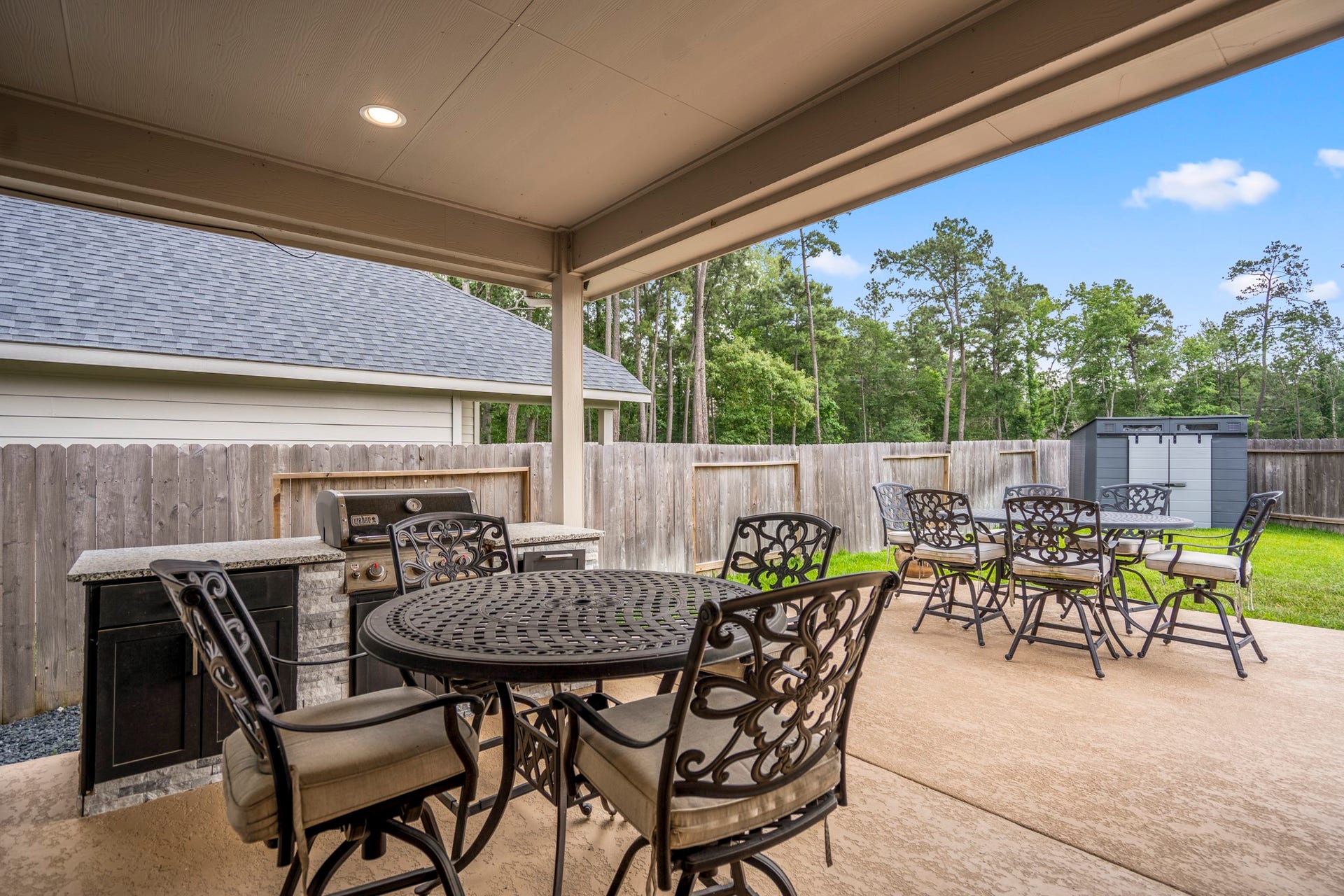 304 Mullins Court, Montgomery, TX 77316 The photo features a spacious covered patio with a built-in grill and overlooks a fenced backyard with a storage shed, offering privacy and a lush tree-lined view.