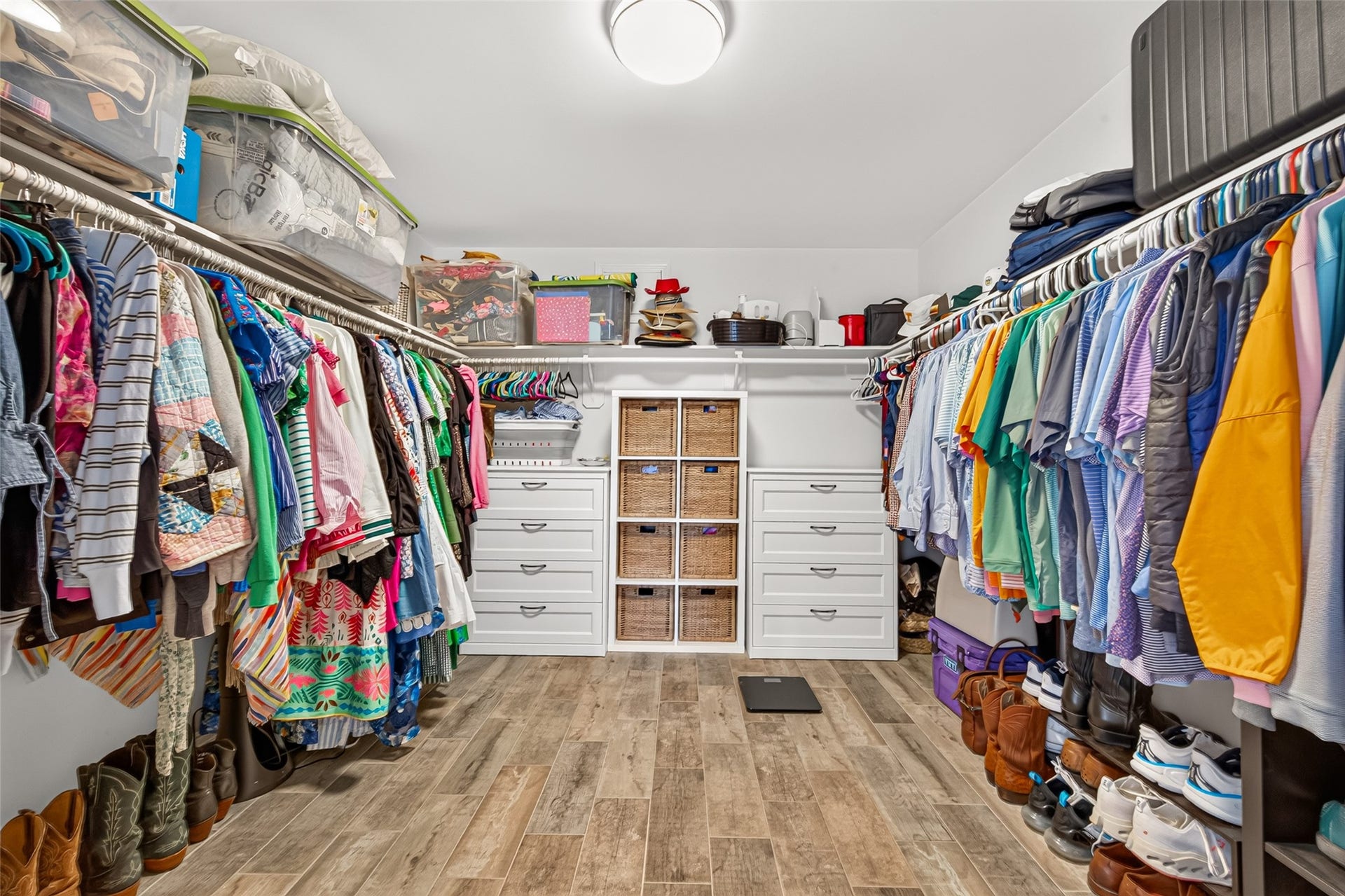 This impressively oversized walk-in primary closet offers a dream setup for organization, storage, and wardrobe display. Continuous multi-tone wood-look plank tile flooring spans the expansive room, creating a seamless and high-end transition from the primary suite.