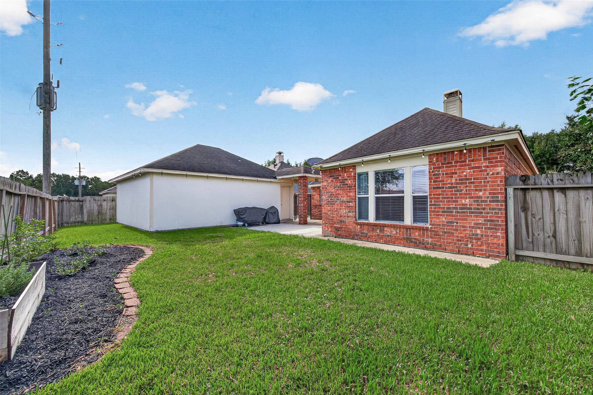 The four-sided brick construction and detached garage layout wrap around the back, creating a secluded courtyard-style patio area. Full wooden privacy fencing frames the perimeter, providing peace of mind and complete seclusion under a wide-open blue sky.