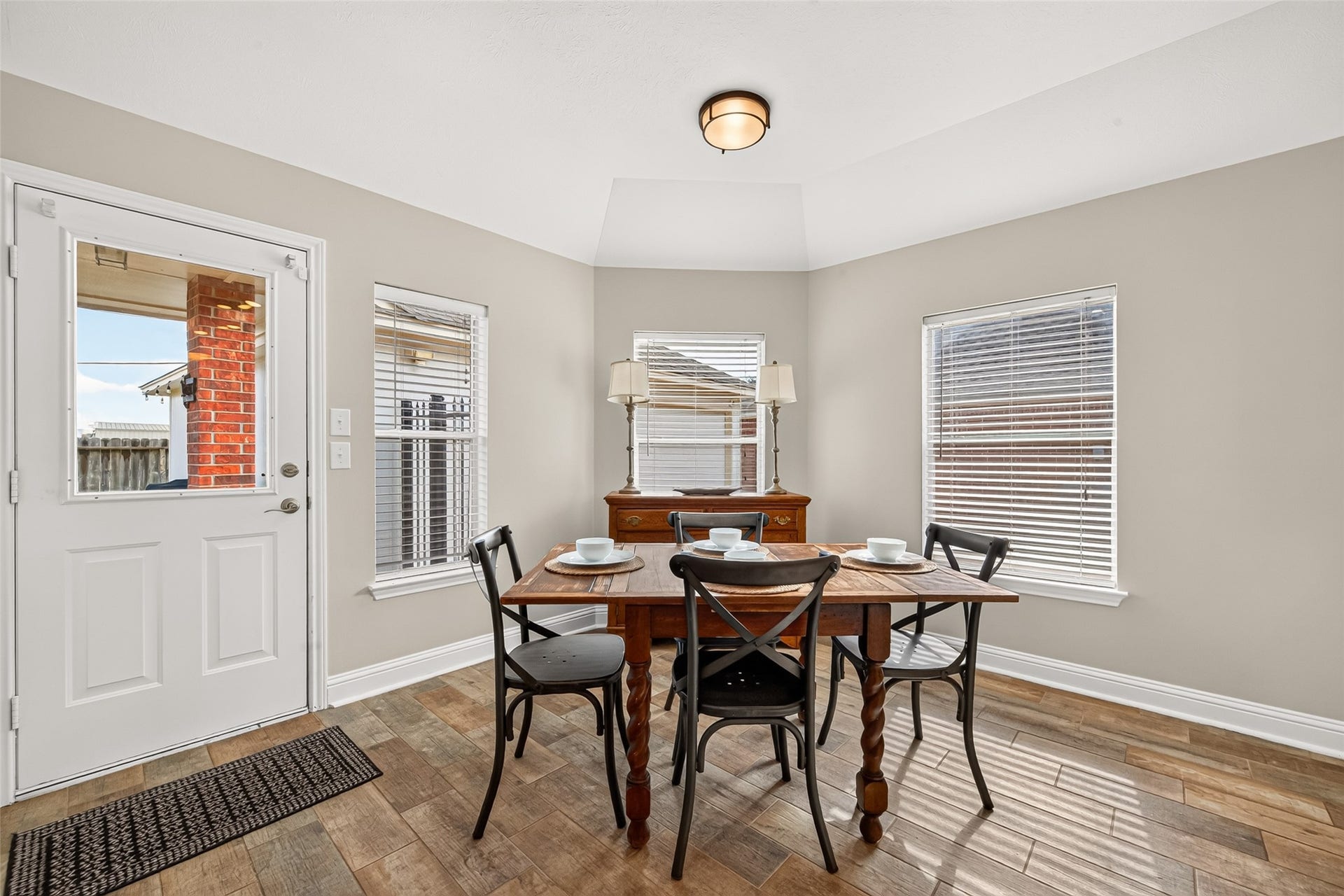 Just steps away from the kitchen with tray ceiling detail and a classic flush-mount light fixture, the dining alcove is bathed in soft natural light pouring through three large, white-blinded windows.