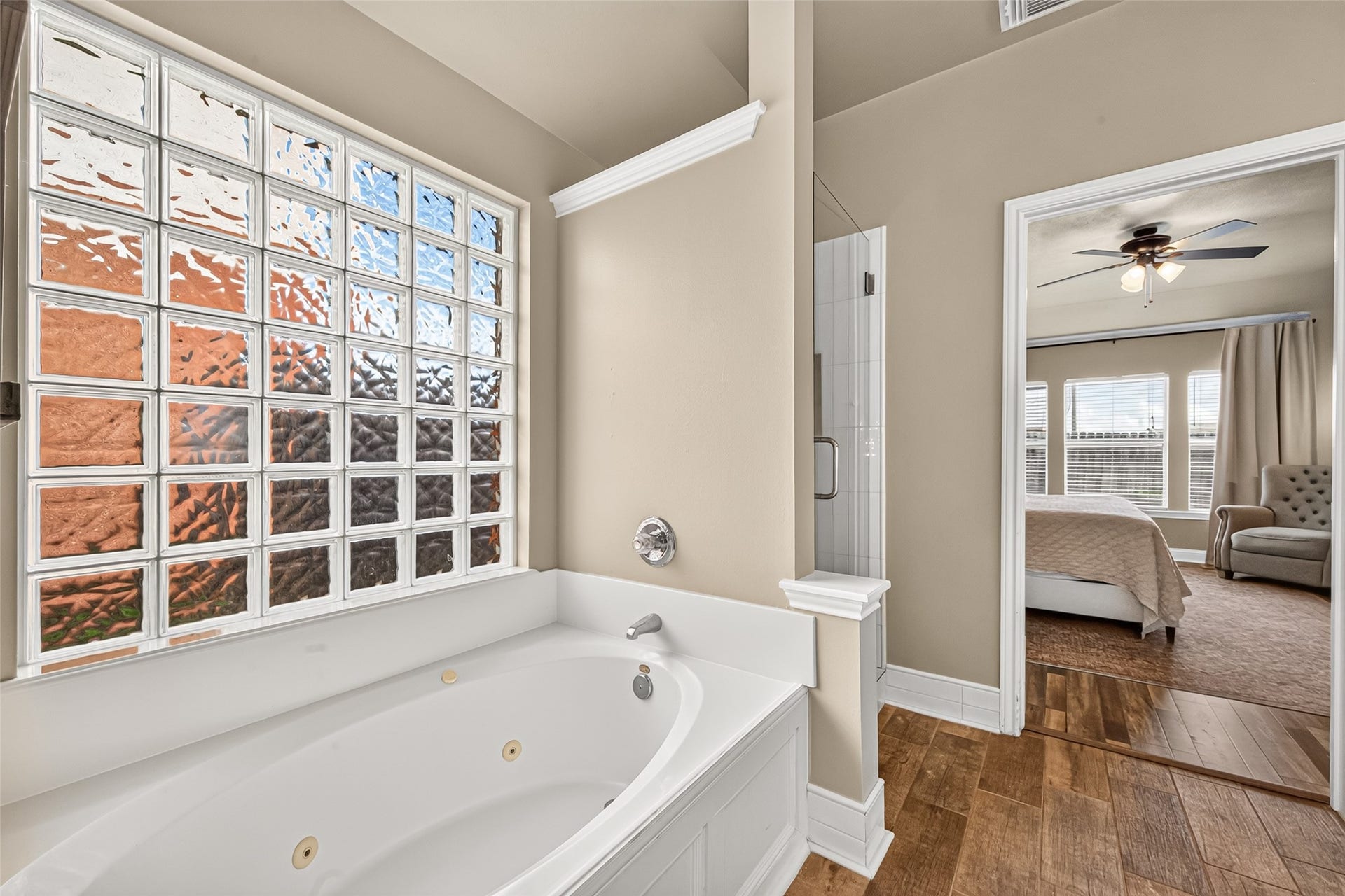 The framed soaking tub features classic white paneling and sits beneath a decorative wooden arched grid mirror on a soothing neutral accent wall.