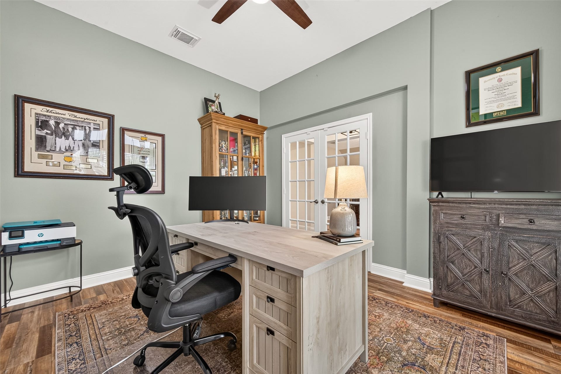 Offering a full view back toward the entrance, this angle highlights the grand, elegant entrance to the home office through white French double doors with glass window panes. The rooms generous proportions effortlessly accommodate large executive furnishings while maintaining an open, airy atmosphere