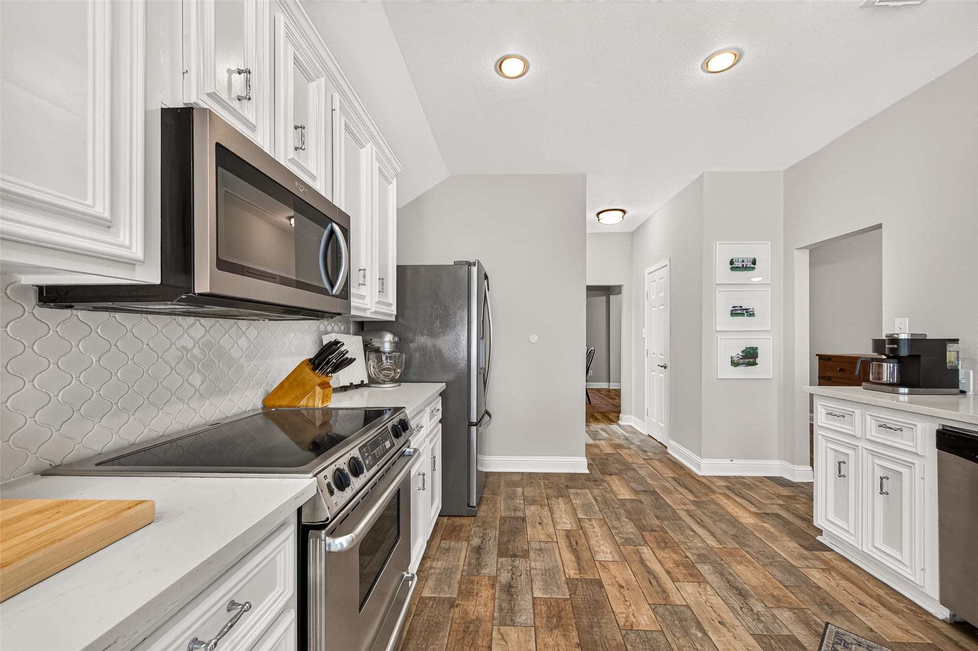 Recessed ceiling lights illuminate the room, while durable wood-look tile flooring flows continuously into the adjoining breakfast nook and sunlit living spaces, ensuring effortless connectivity throughout the home.