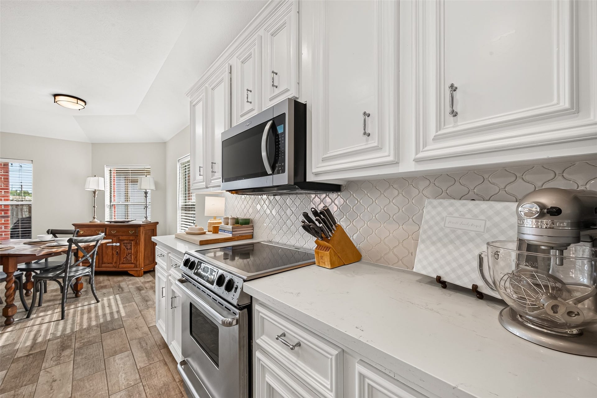 Modernized with crisp white raised-panel cabinetry, smooth solid-surface countertops, and a stylish arabesque tile backsplash, the space combines timeless elegance with exceptional functionality.