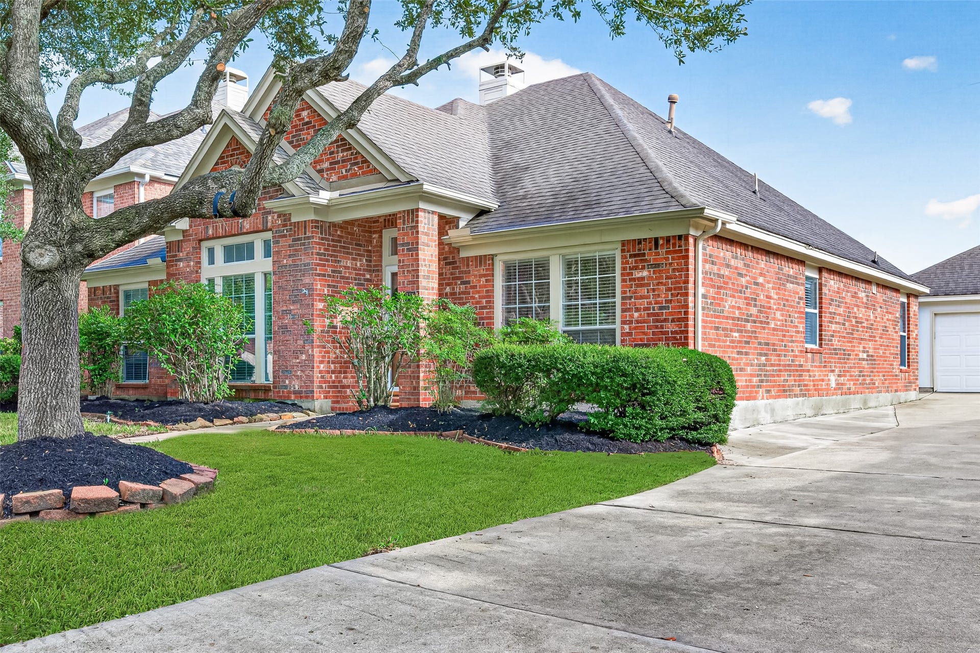 A central concrete walkway splits the green front lawn, guiding the eye toward a wood-toned front door fitted with a decorative green wreath, glass panels, a storm door, and framed by glass sidelights and a top transom window.