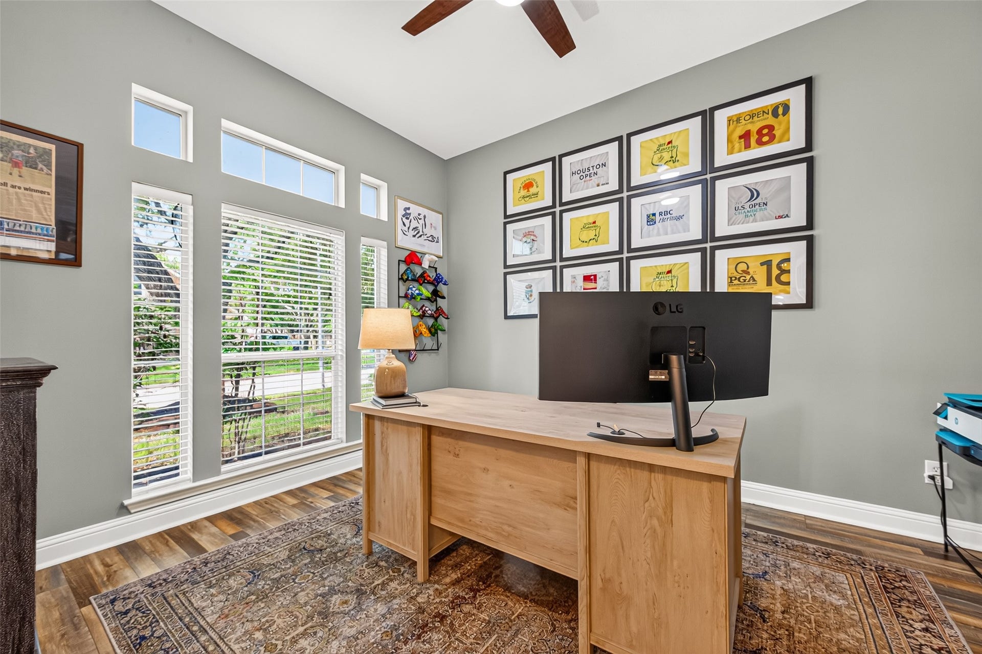 This home office just off the main entryway is bathed in exceptional natural light, the space features a striking wall of floor-to-ceiling multi-pane windows topped with custom transom accents, offering peaceful views of the lush front lawn and shade trees.