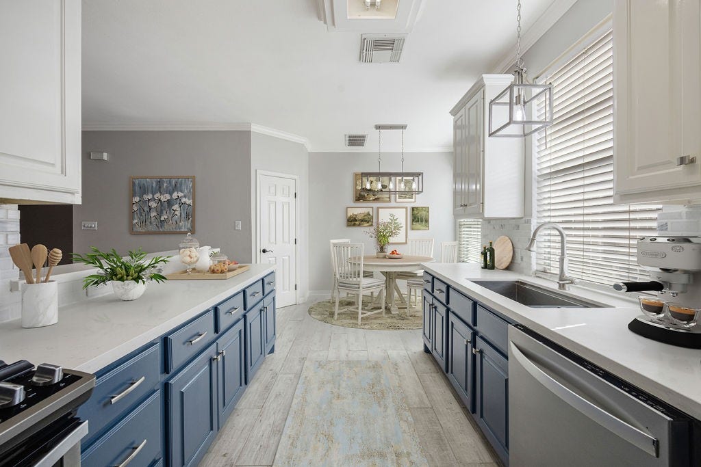A galley kitchen with serious presence. Bold lower cabinetry, long prep space, and open sightlines into the breakfast nook and main living area. Image has been virtually staged.