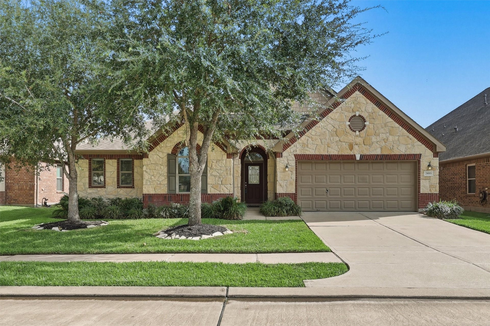 24015 Orange Orchard Lane, Katy, TX 77493 Stone and brick under a mature live oak in Katy Oaks, with a two-car garage and a deep front lawn - an established street with the shade a new subdivision is still waiting on.