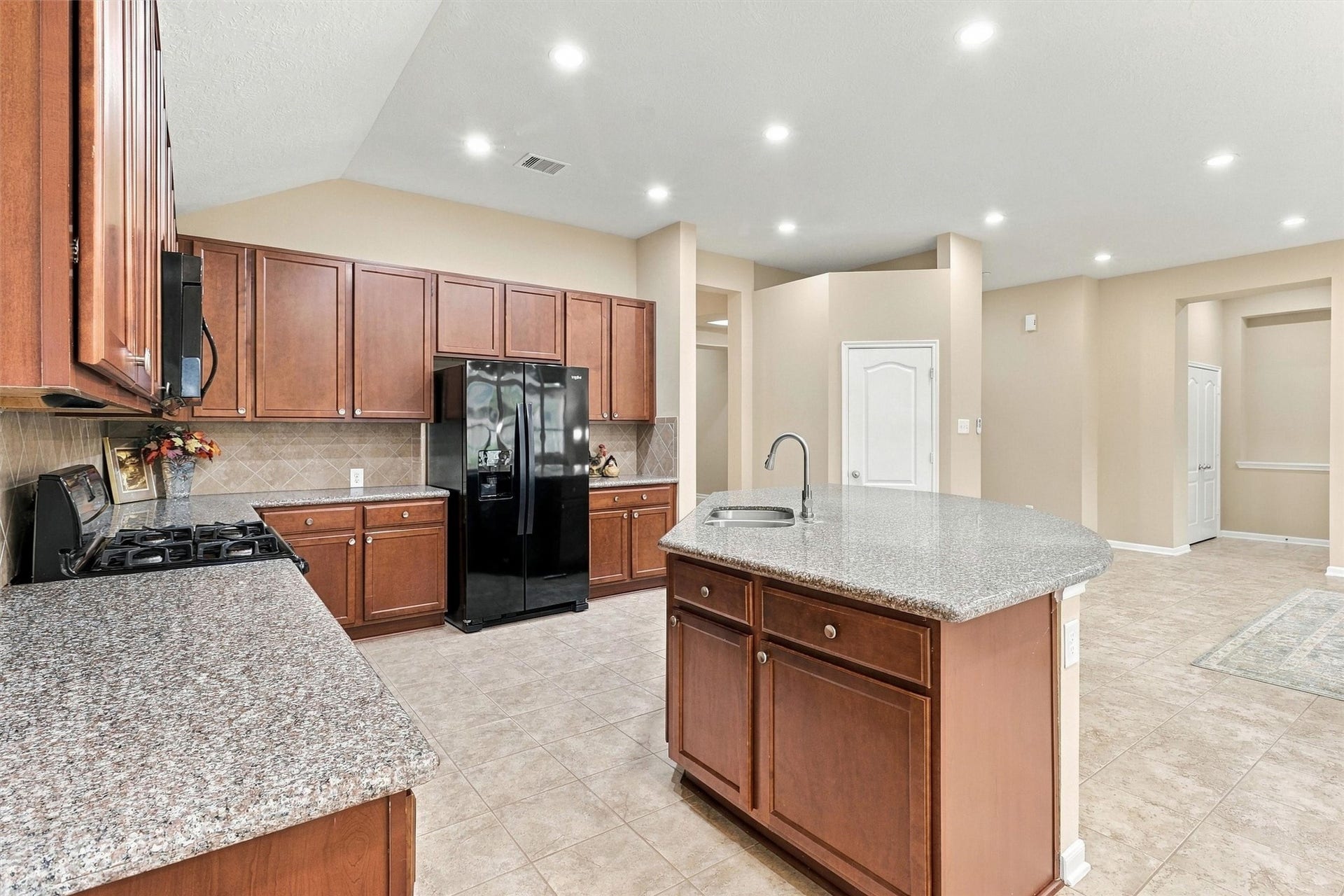 24015 Orange Orchard Lane, Katy, TX 77493 A gas range and matching built-in microwave from Whirlpool sit under a tile backsplash, framed by 42-inch birch cabinets and granite counters.
