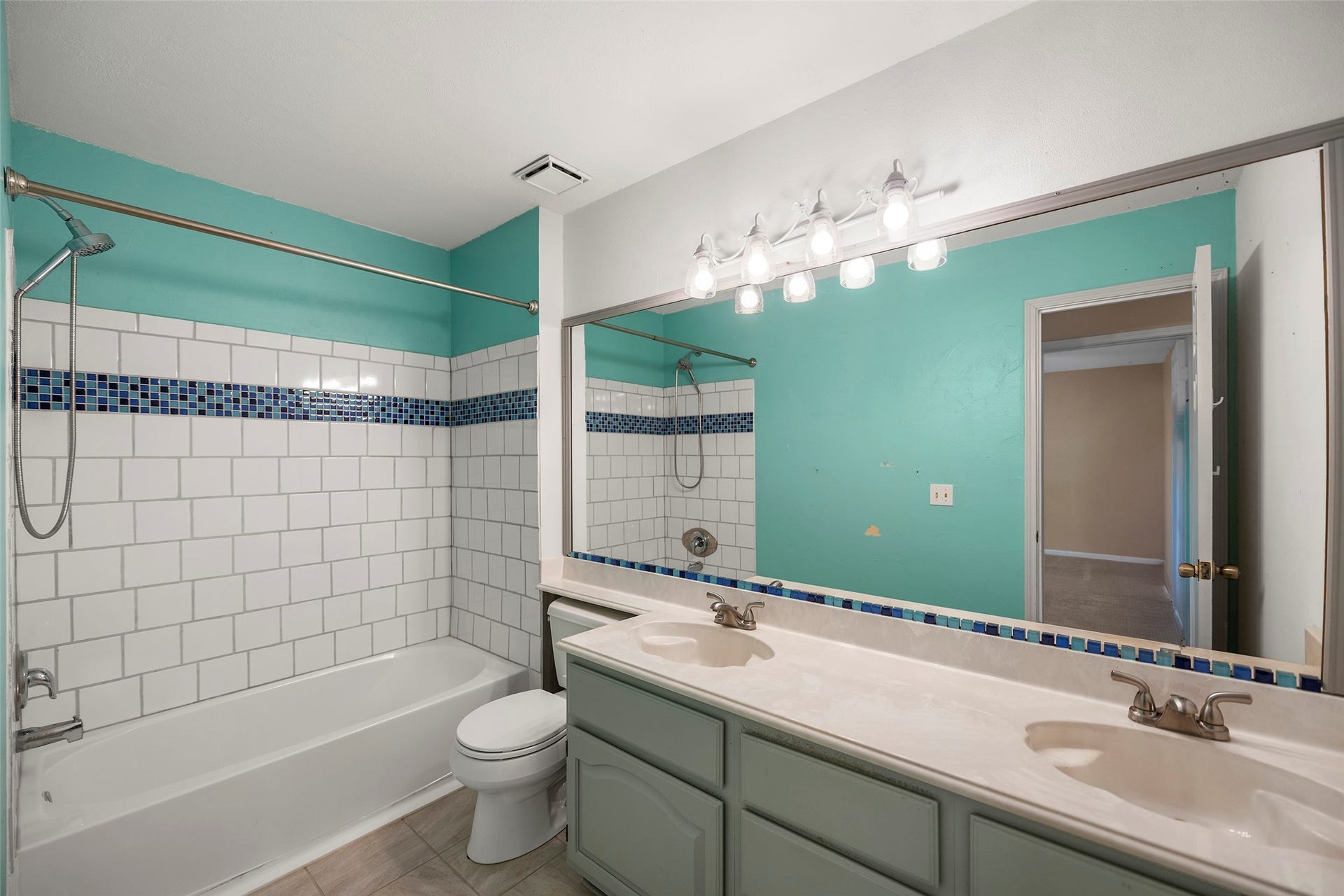 2631 Woodsboro Drive, Spring, TX 77388 Bright and inviting bathroom featuring a double vanity with modern lighting, vibrant teal walls, and a classic bathtub with a stylish tile backsplash.