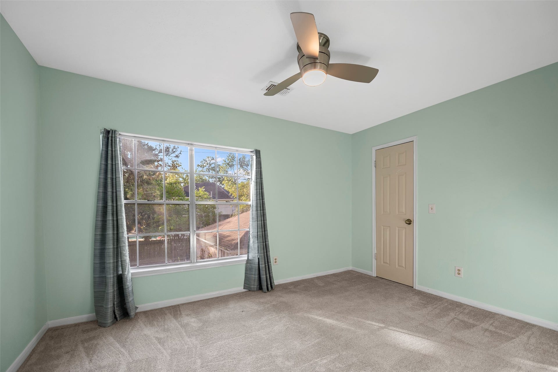 2631 Woodsboro Drive, Spring, TX 77388 Bright and airy bedroom featuring soft mint green walls, a large window with lush outdoor views, and a modern ceiling fan for comfort.